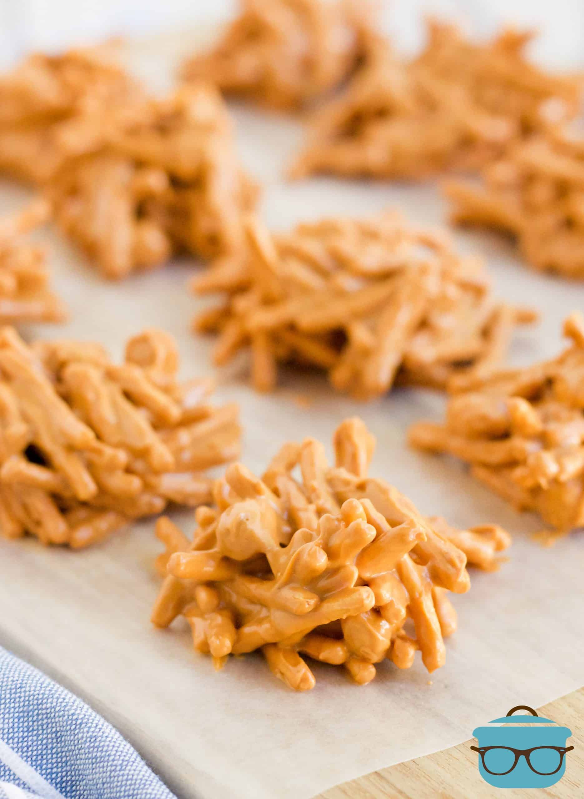 No-Bake butterscotch peanut chow mein candy treats cooling on wax paper that is on a light wood cutting board.