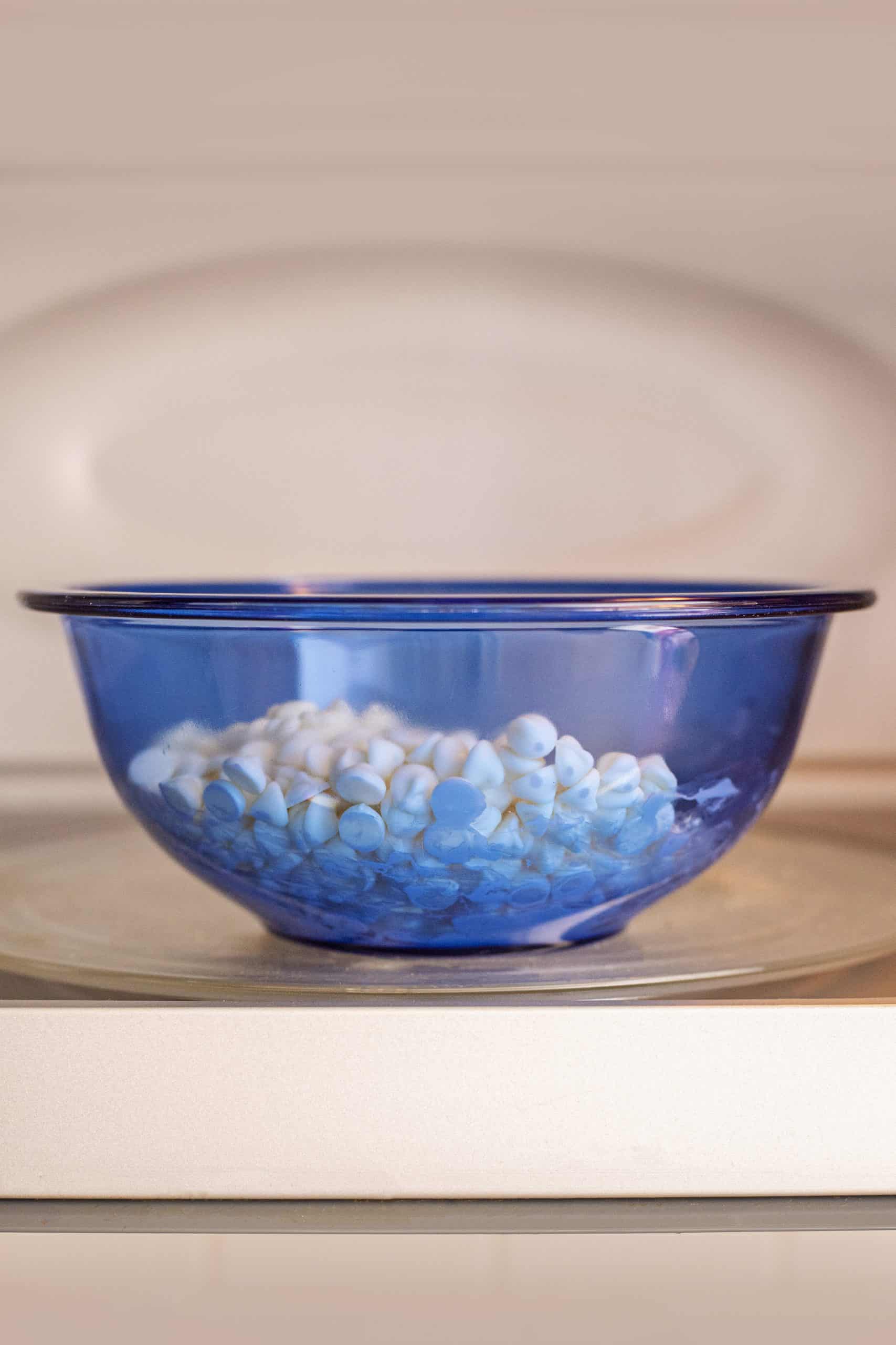 white chocolate chips in a blue bowl inside the microwave.