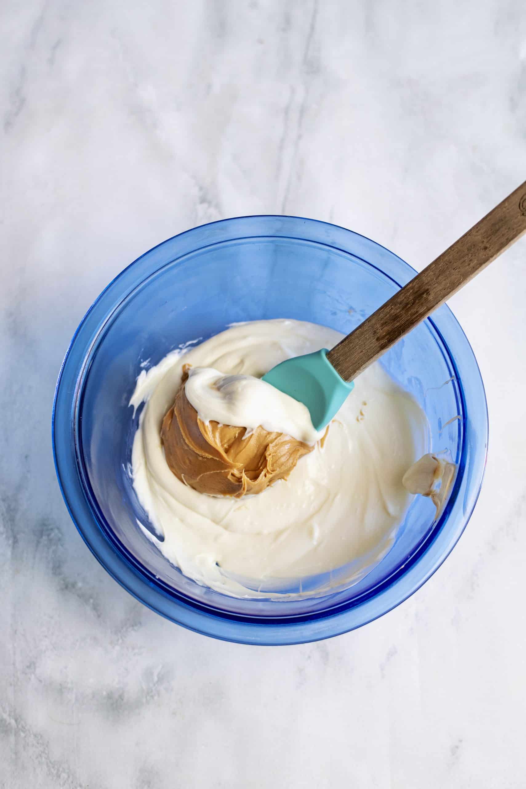 stirring peanut butter into melted white chocolate in a blue bowl.