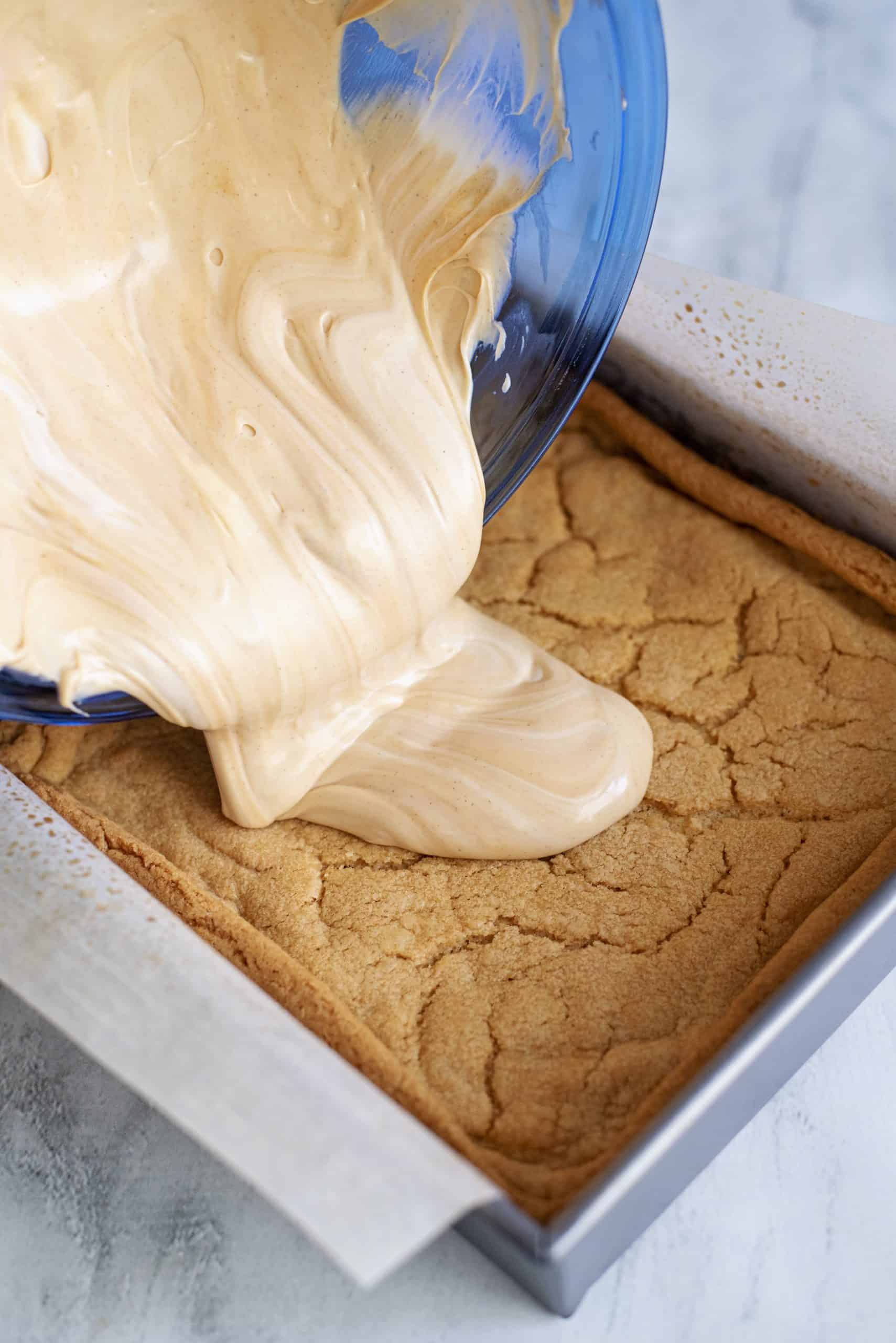pouring peanut butter white chocolate over baked sugar cookie bars.
