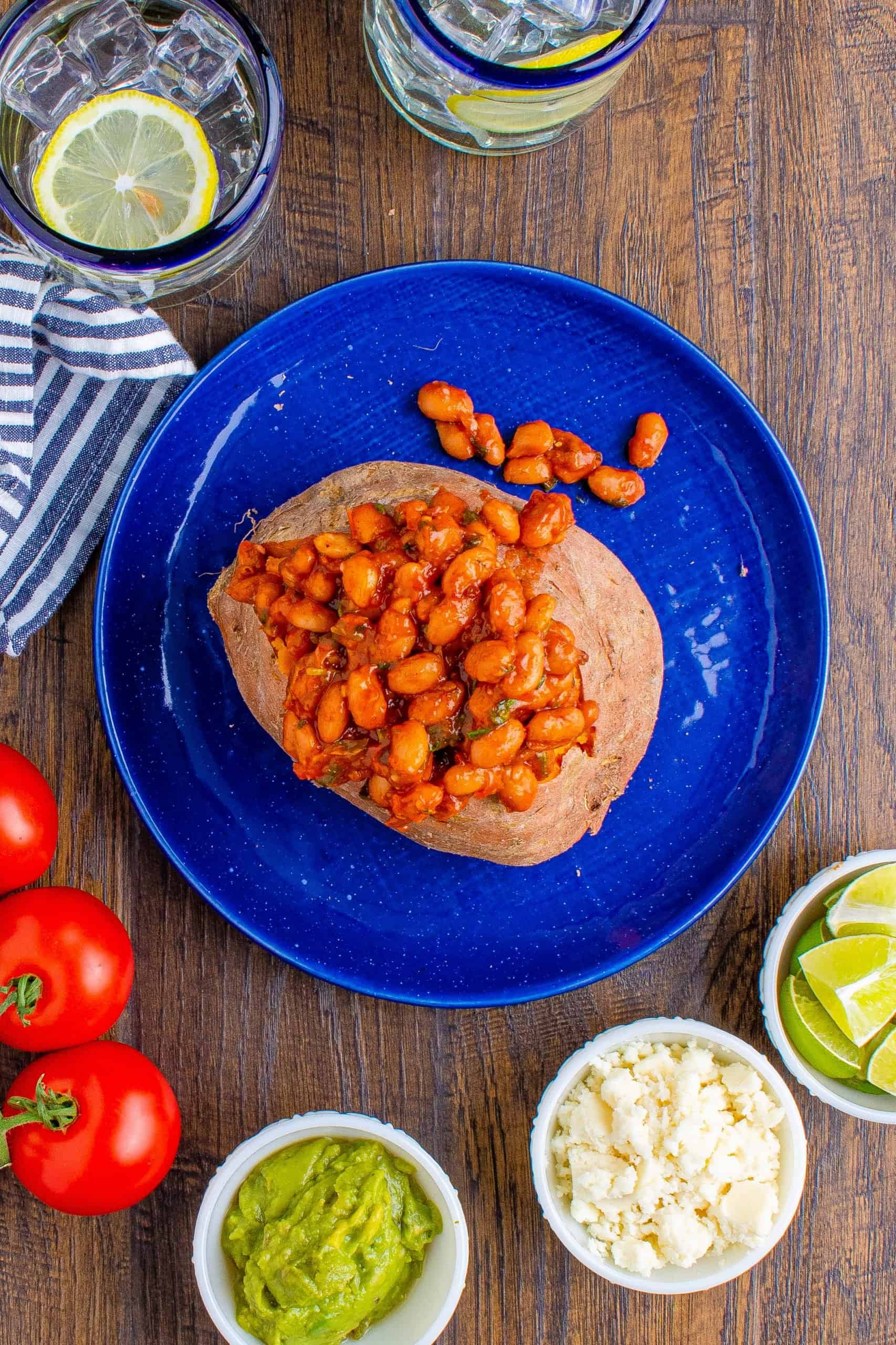 taco seasoned pinto bean mixture added inside cooked sweet potato on a blue plate.
