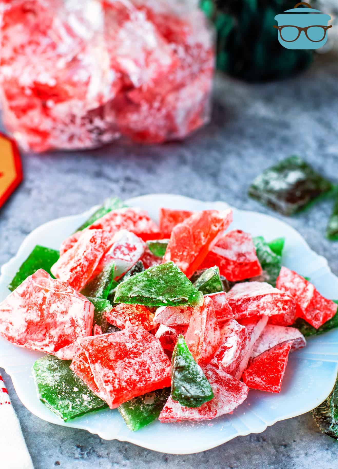 pieces of red and green rock candy shown on a white plate with a bag od red candy in the background.
