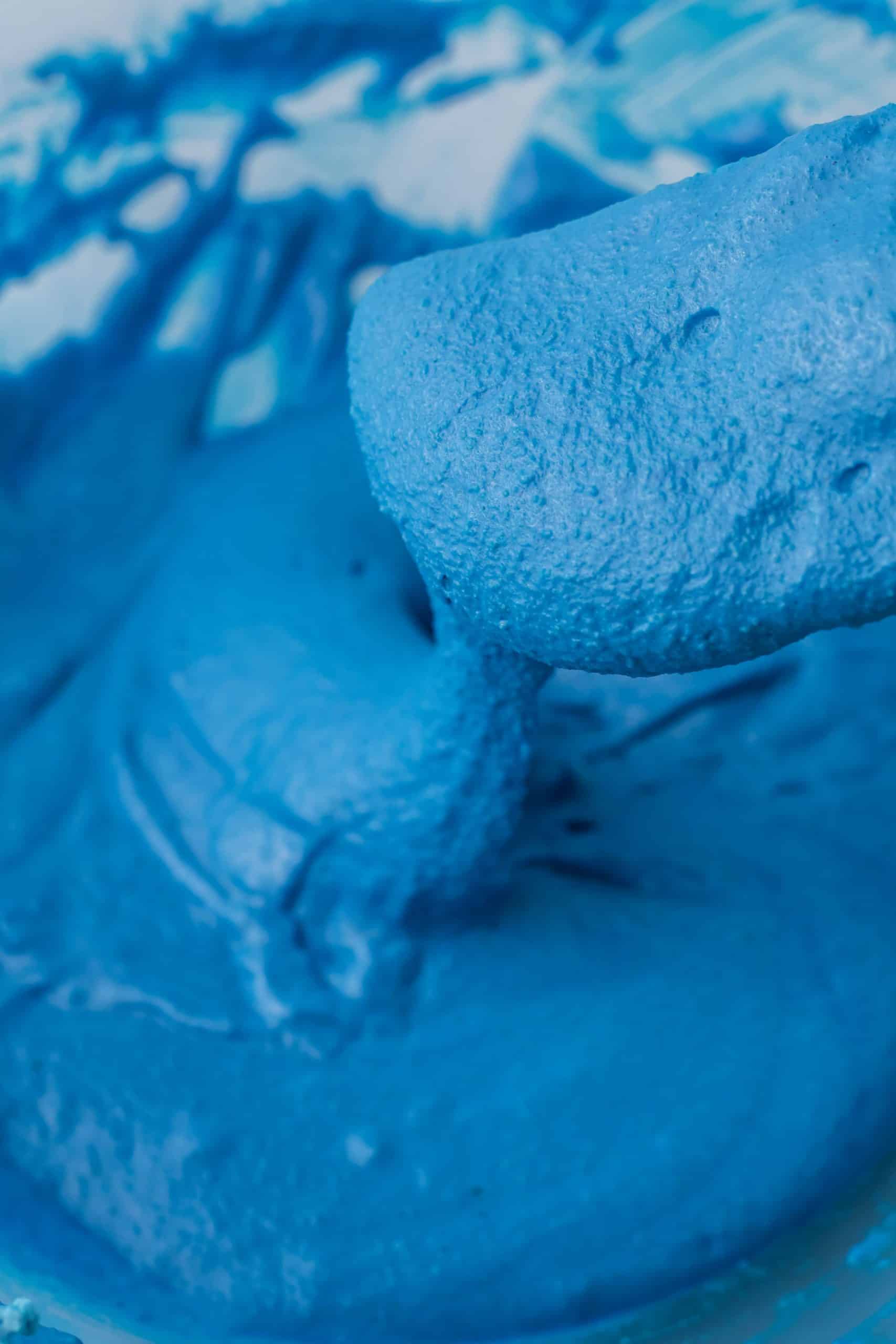 bright blue macaron batter being shown on a spatula in a bowl.