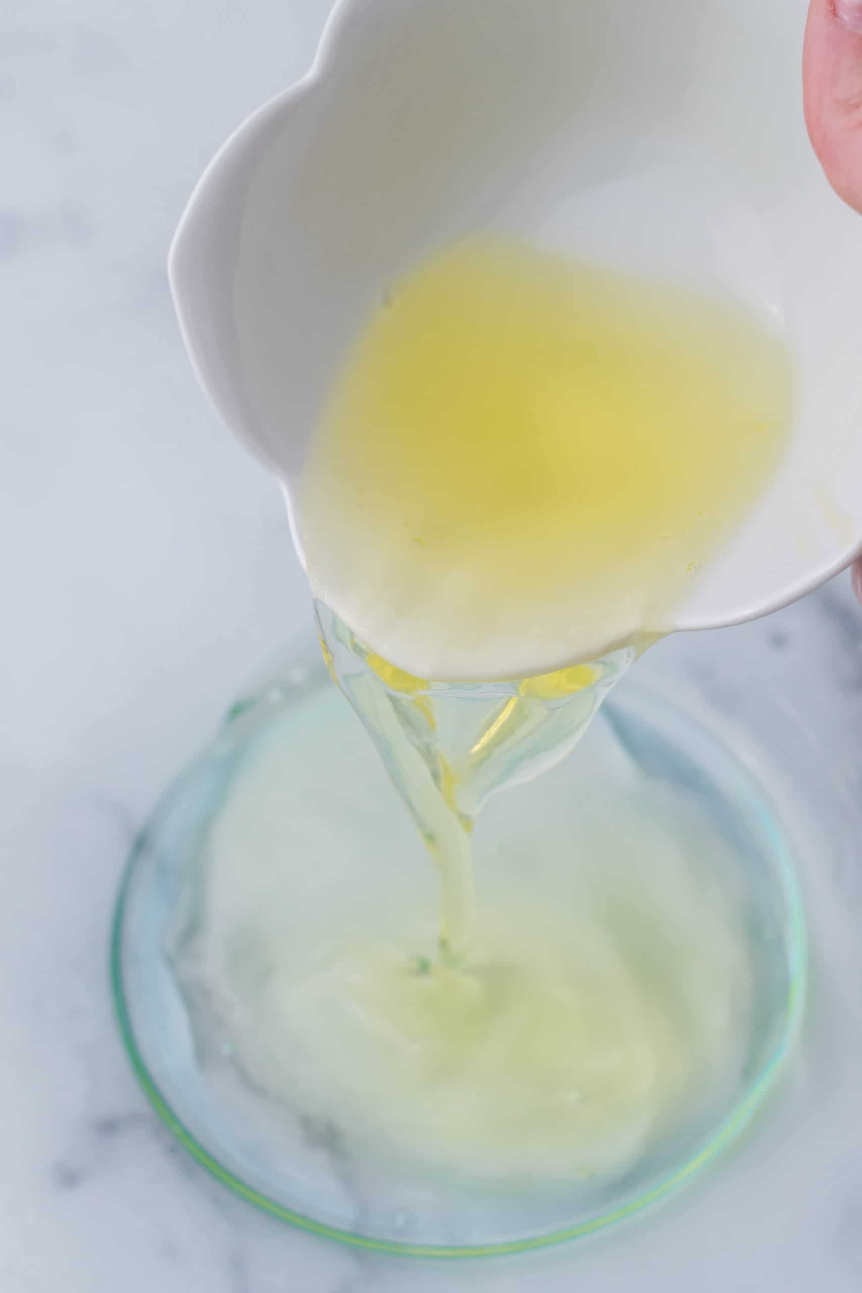 egg yolks being poured from a small white bowl in a larger clear bowl.