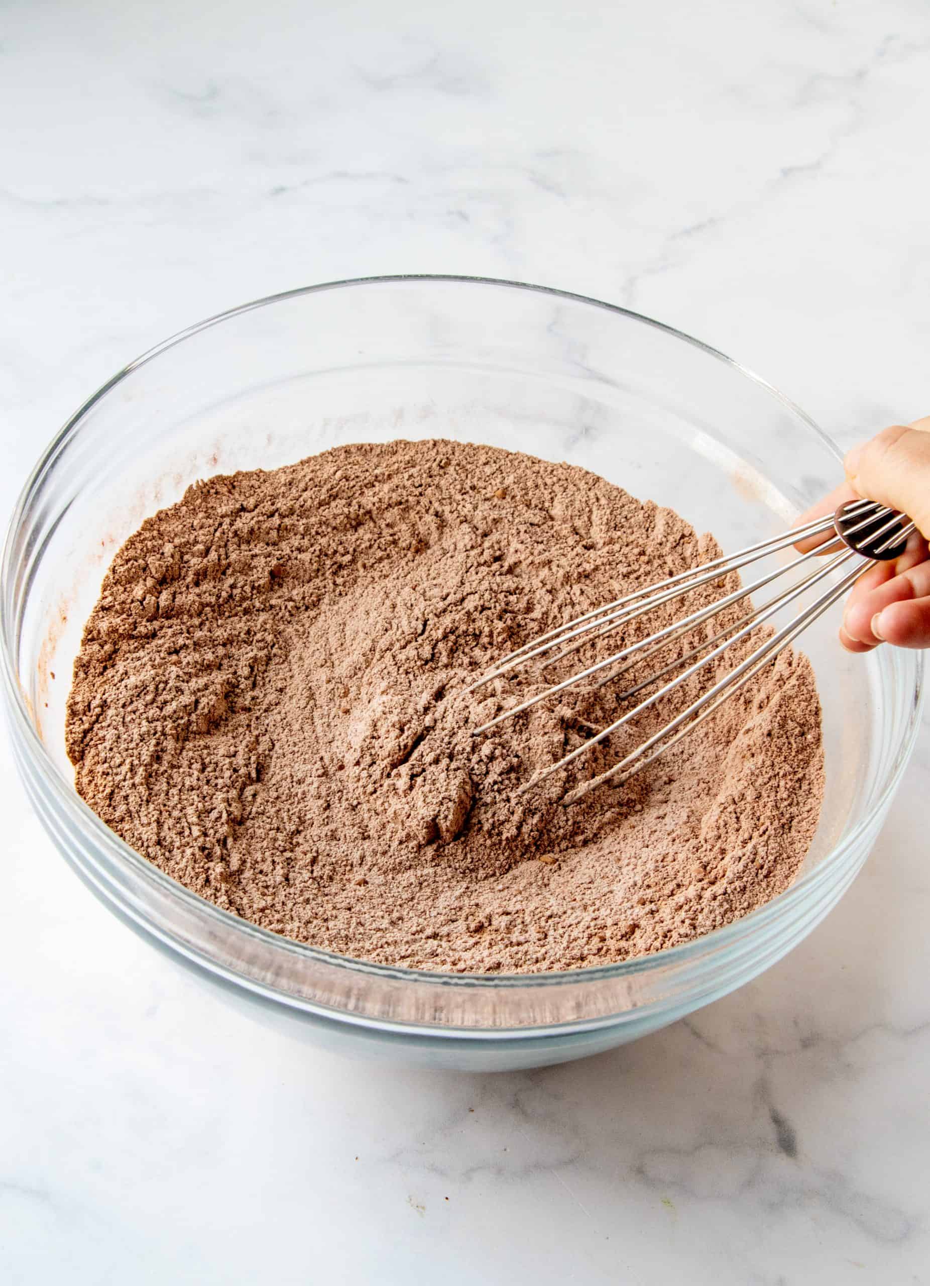 chocolate cake dry ingredients shown being whisked together in a clear bowl.