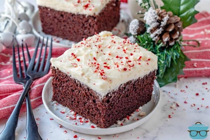 Homemade Chocolate Peppermint Cake, slice of cake shown on a small white round plate with christmas decor the background.