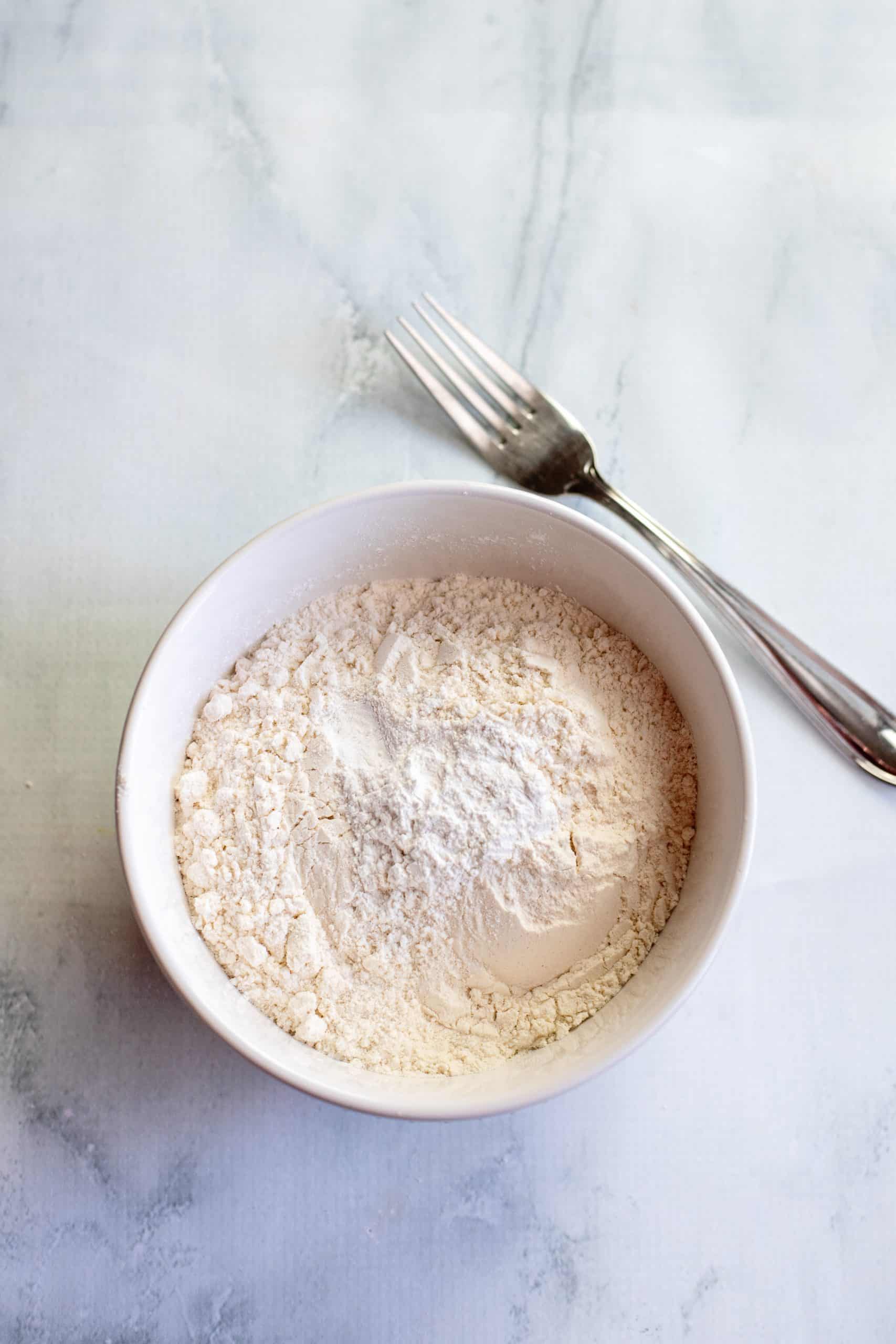 flour, baking powder and salt in a white bowl with a fork on the side.