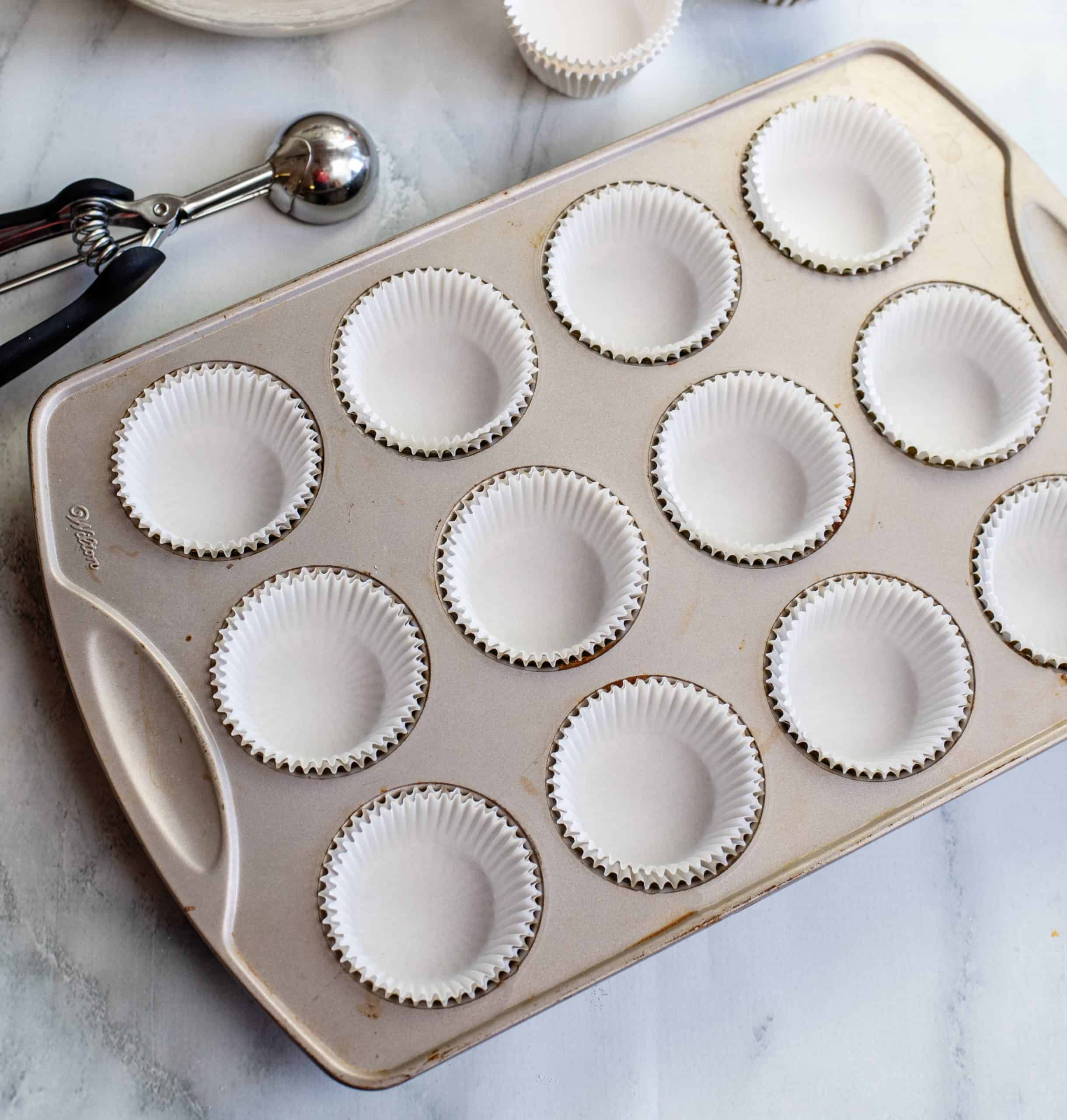 paper liners added to the cupcake pan with a scooper off to the side.