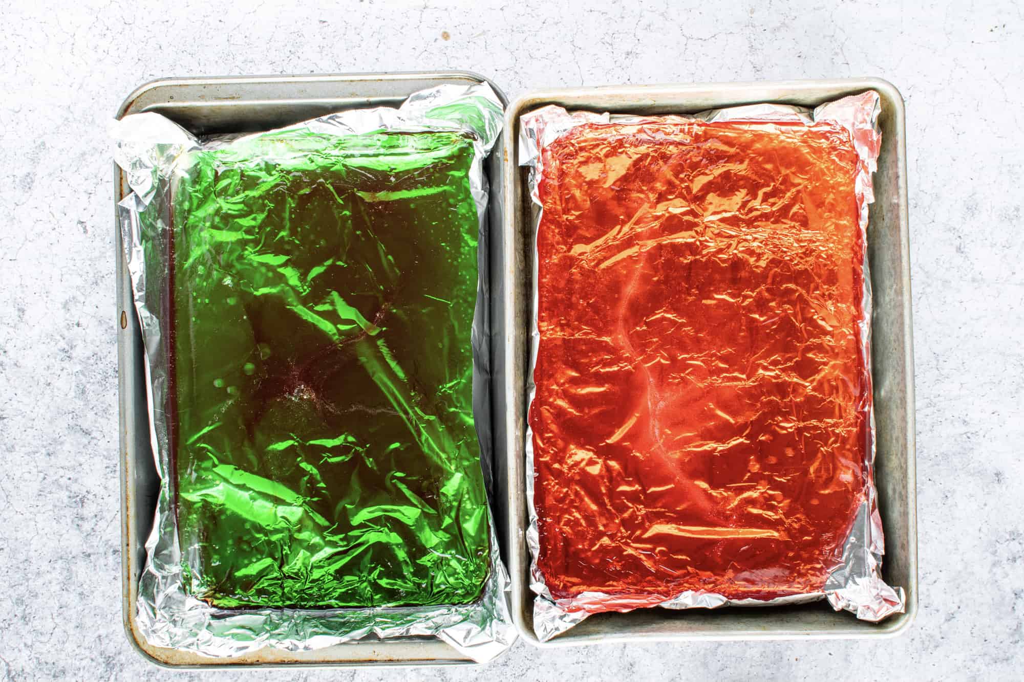red and green liquid rock candy poured into two separate pans lined with aluminum foil.