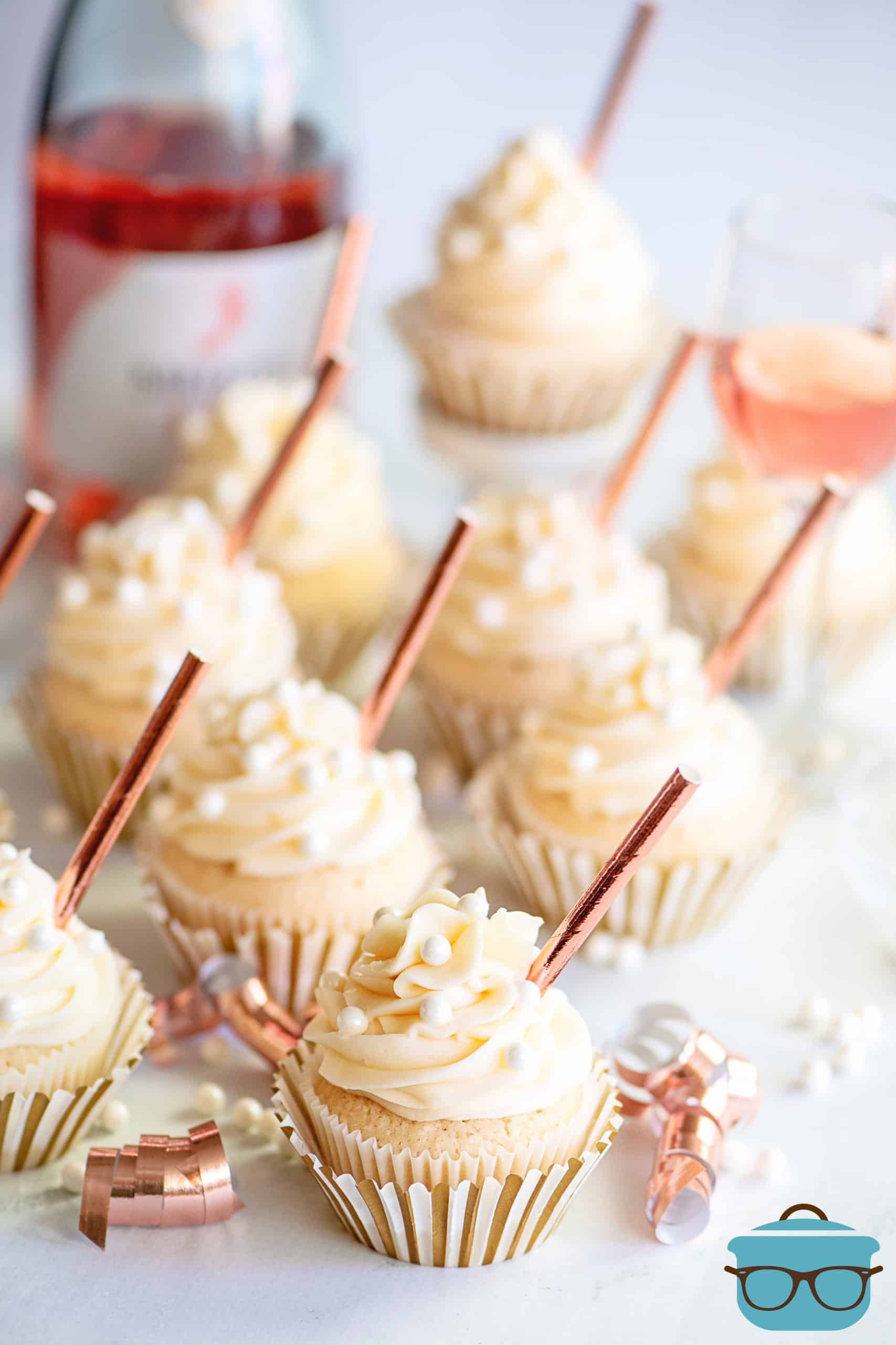 Decorated champagne cupcakes on a granite countertop with a bottle of pink champagne in the background.