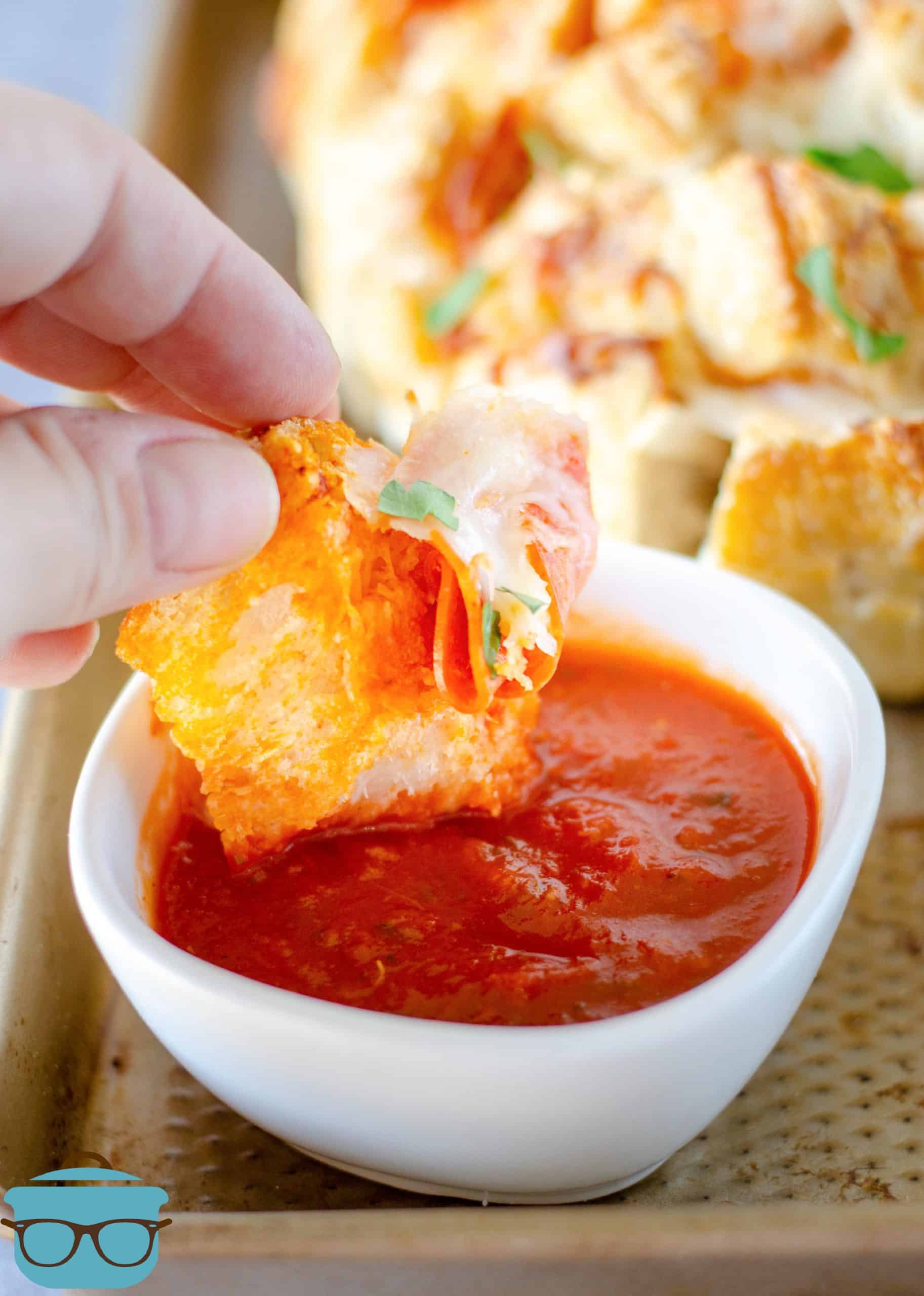 a slice of pepperoni bread being dipped in pizza sauce that is in a small white bowl.