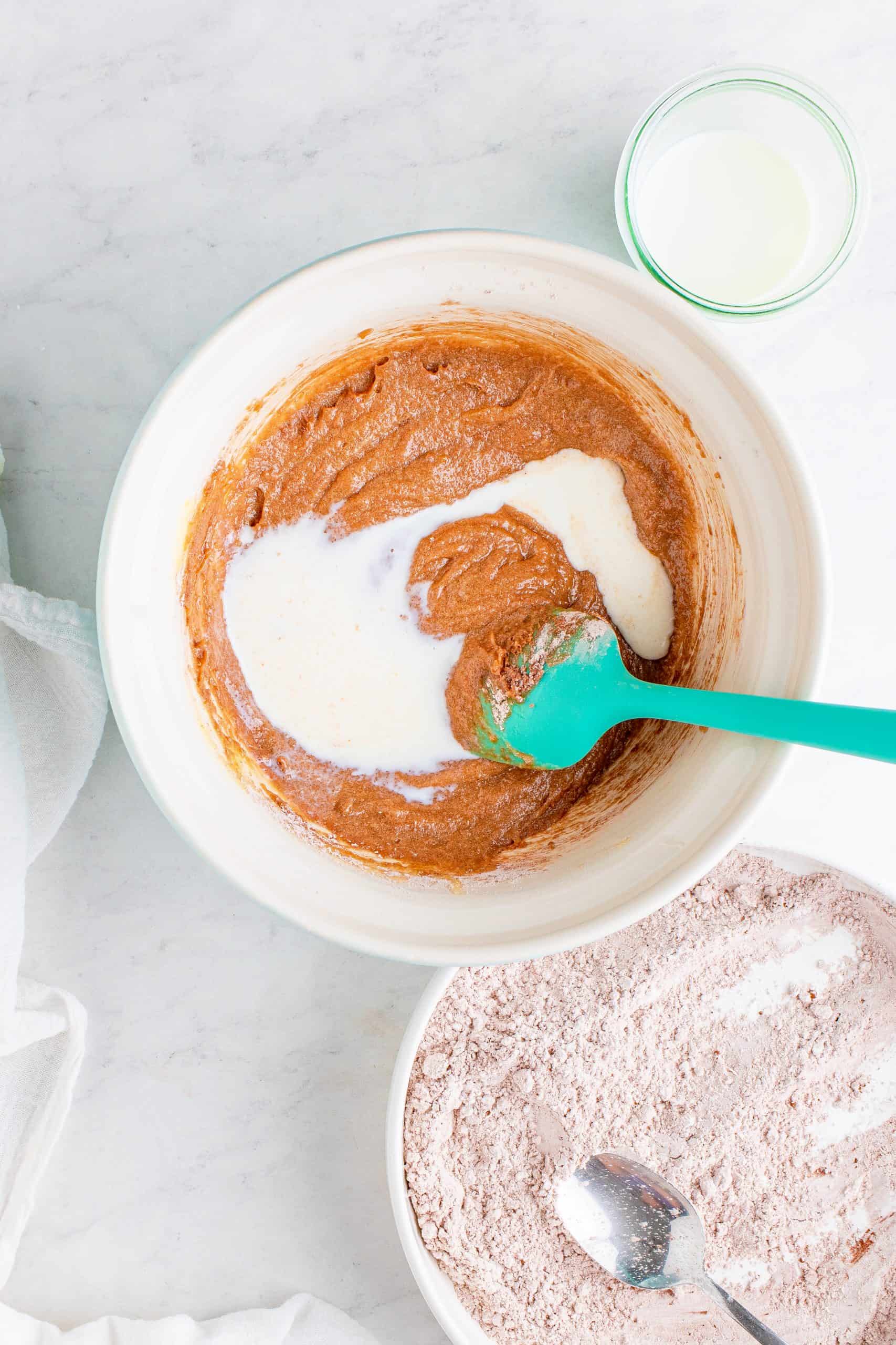 buttermilk added to cocoa batter mixture in a white bowl with a turquoise colored spoon.