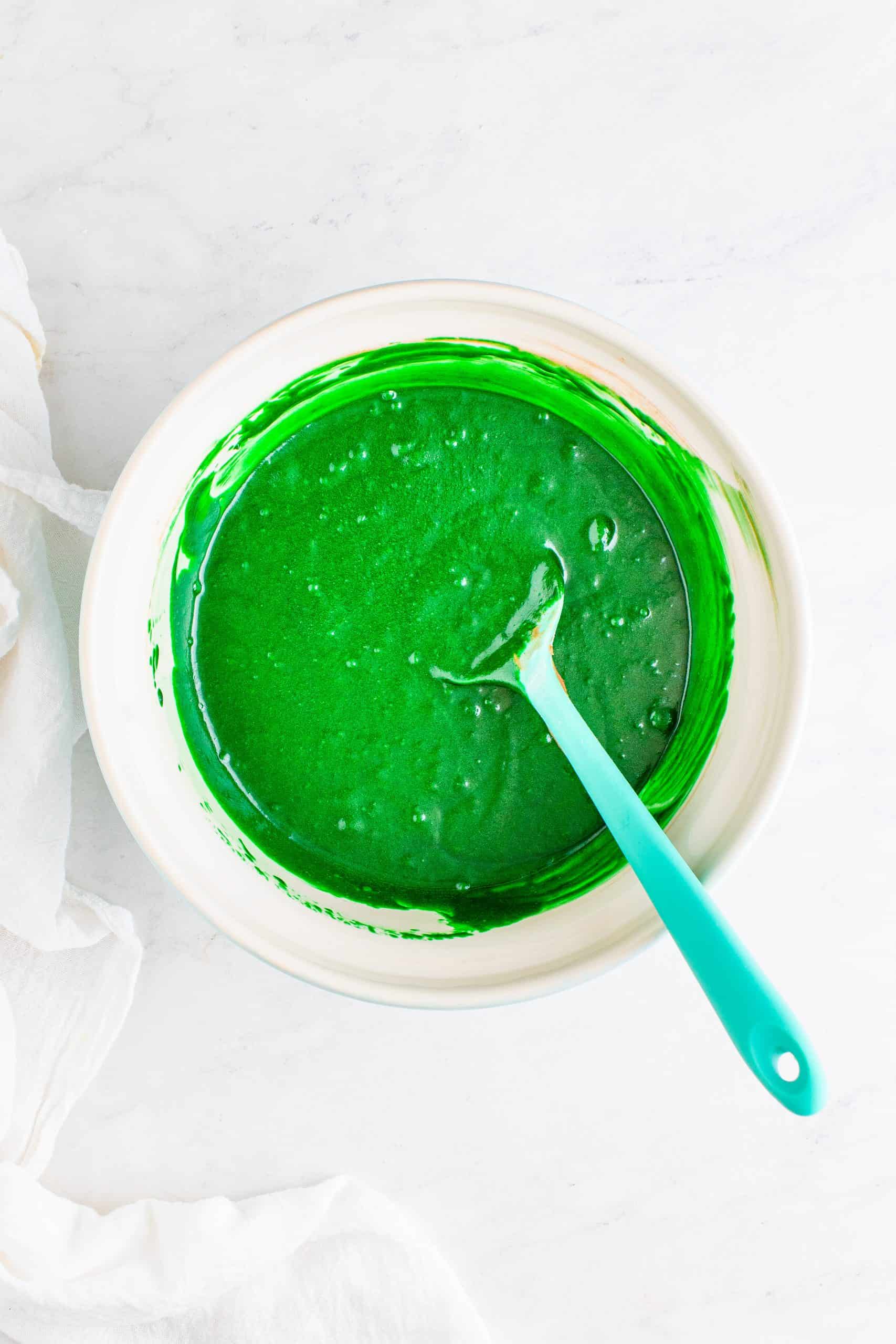 green food coloring added to cocoa cupcake batter in a white bowl.