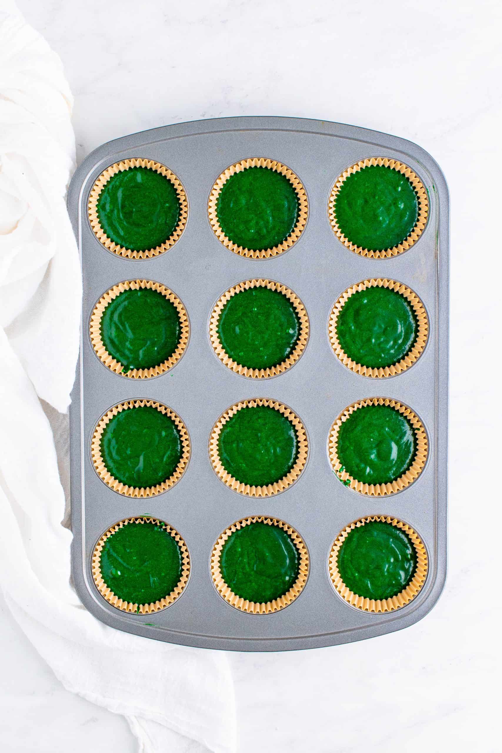muffin tin with cupcake liners filled with green velvet cupcake batter.