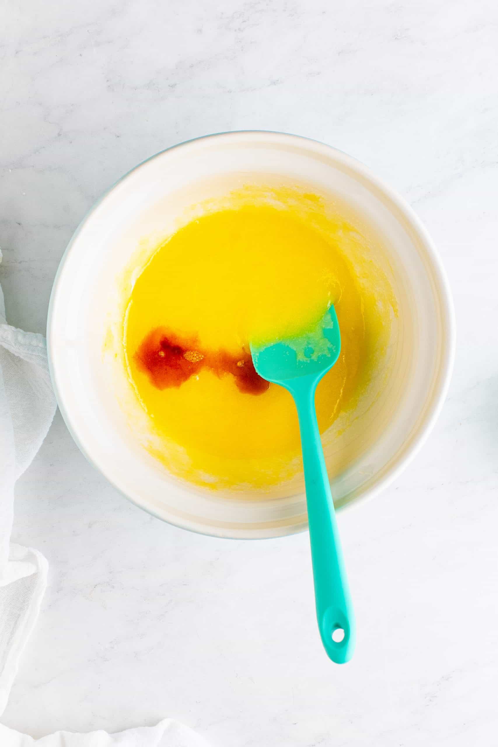 vanilla extract added to melted butter and sugar mixture in a white bowl.