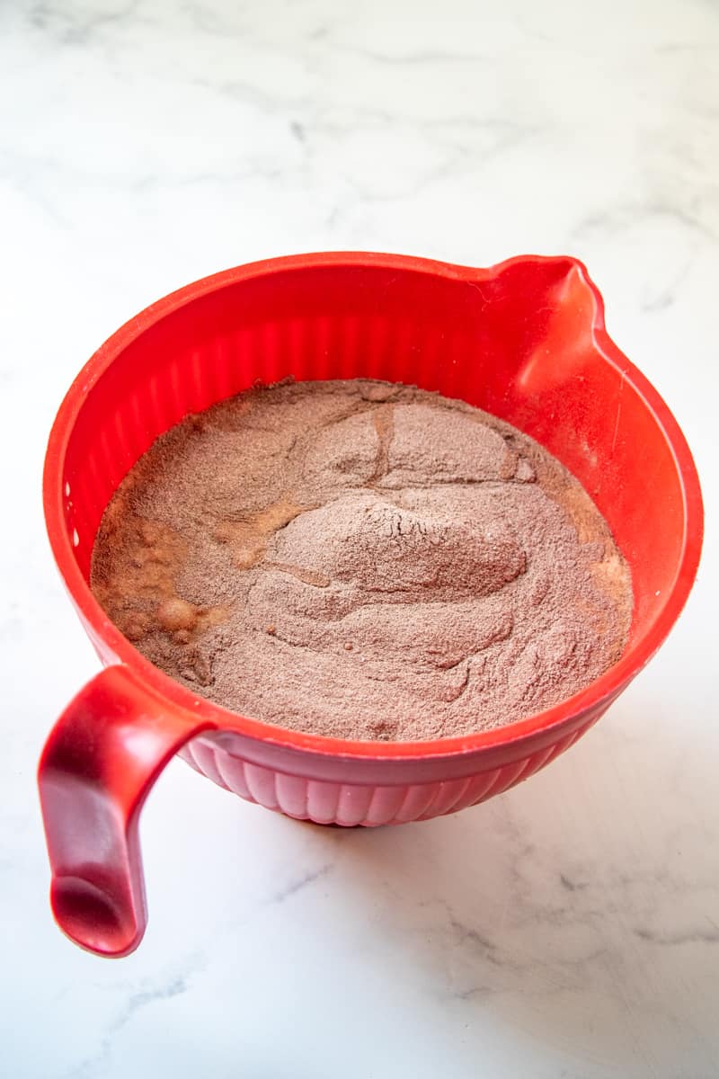 milk, heavy cream, eggs, sugar, hot chocolate powder in a red mixing bowl sitting on a marble surface.