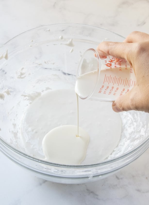 pouring heavy cream from a measuring cup into marshmallow fluff.