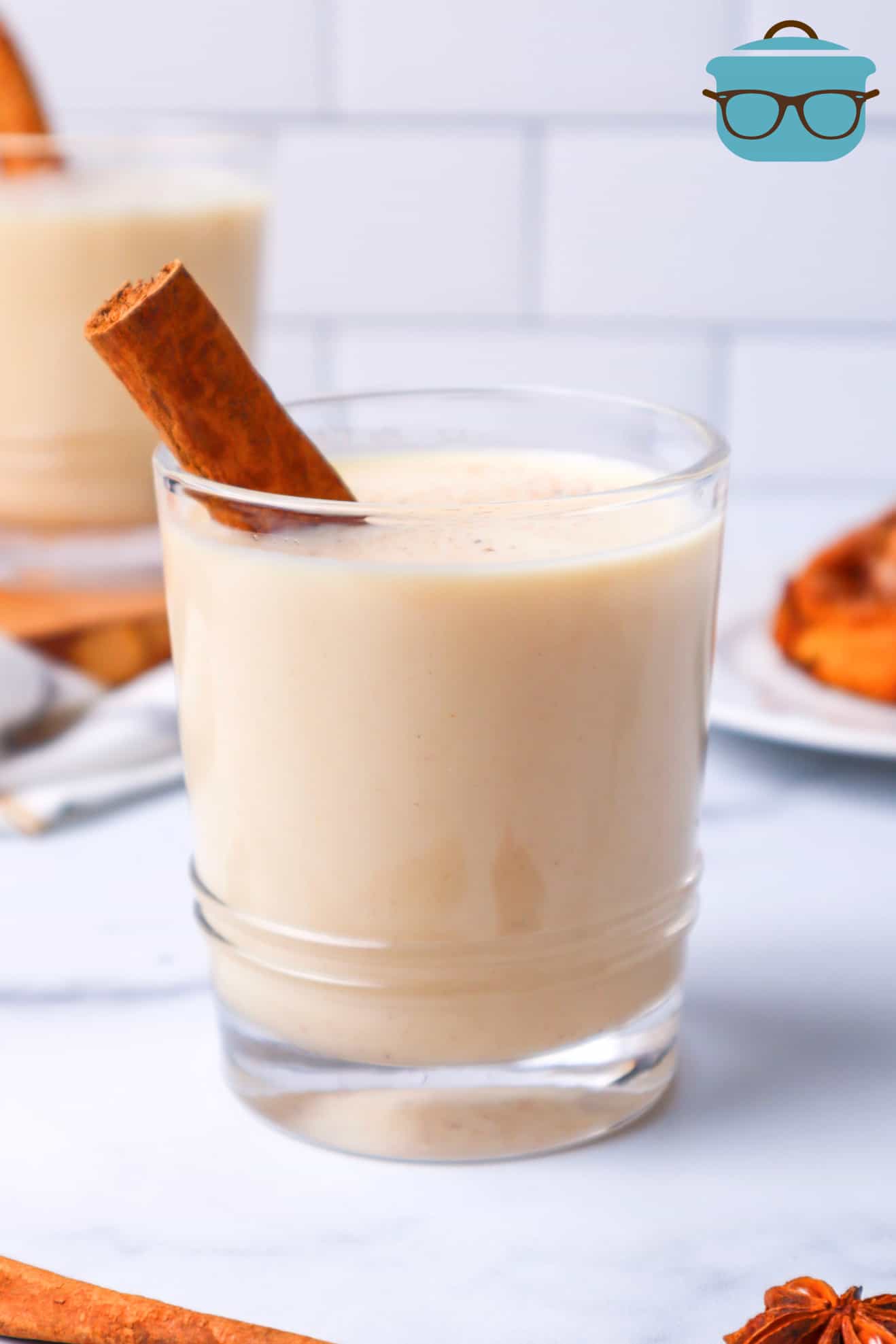 glass of egg nog with cinnamon stick shown in front of a white background.