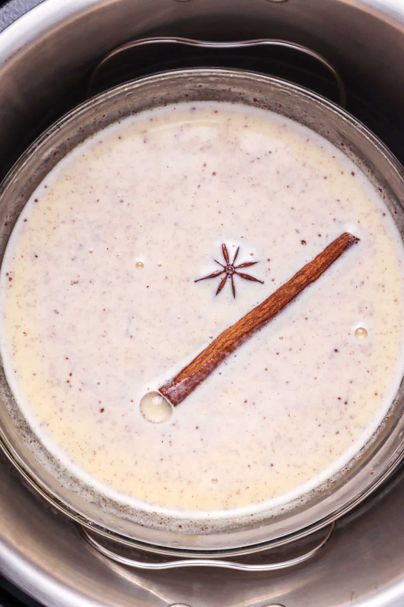 cinnamon stick and star anise floating in egg, sugar, cream mixture shown inside the pressure cooker.
