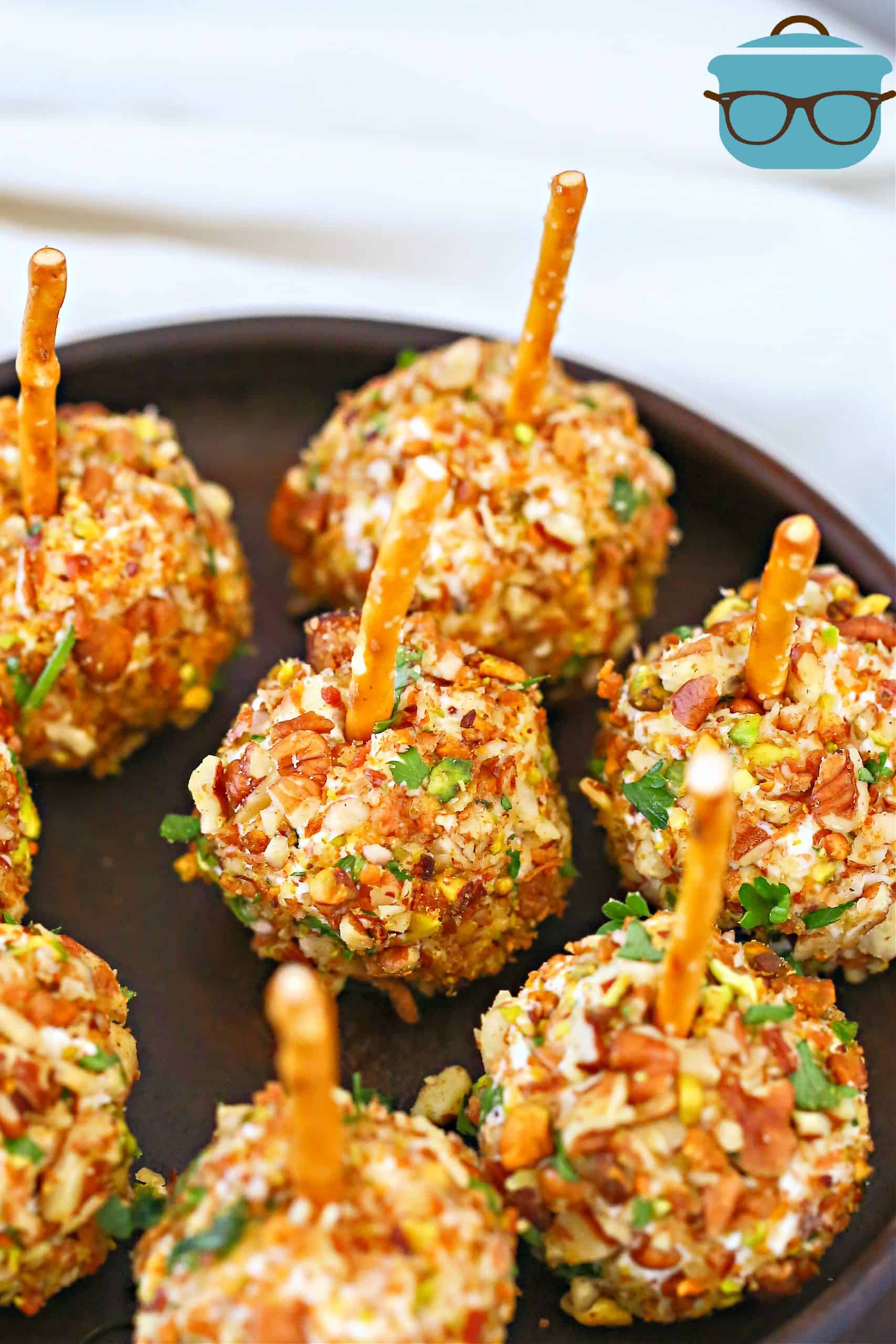 Easy Mini Pecan Coated Cheeseball appetizers with pretzel sticks shown on a black, circle platter.