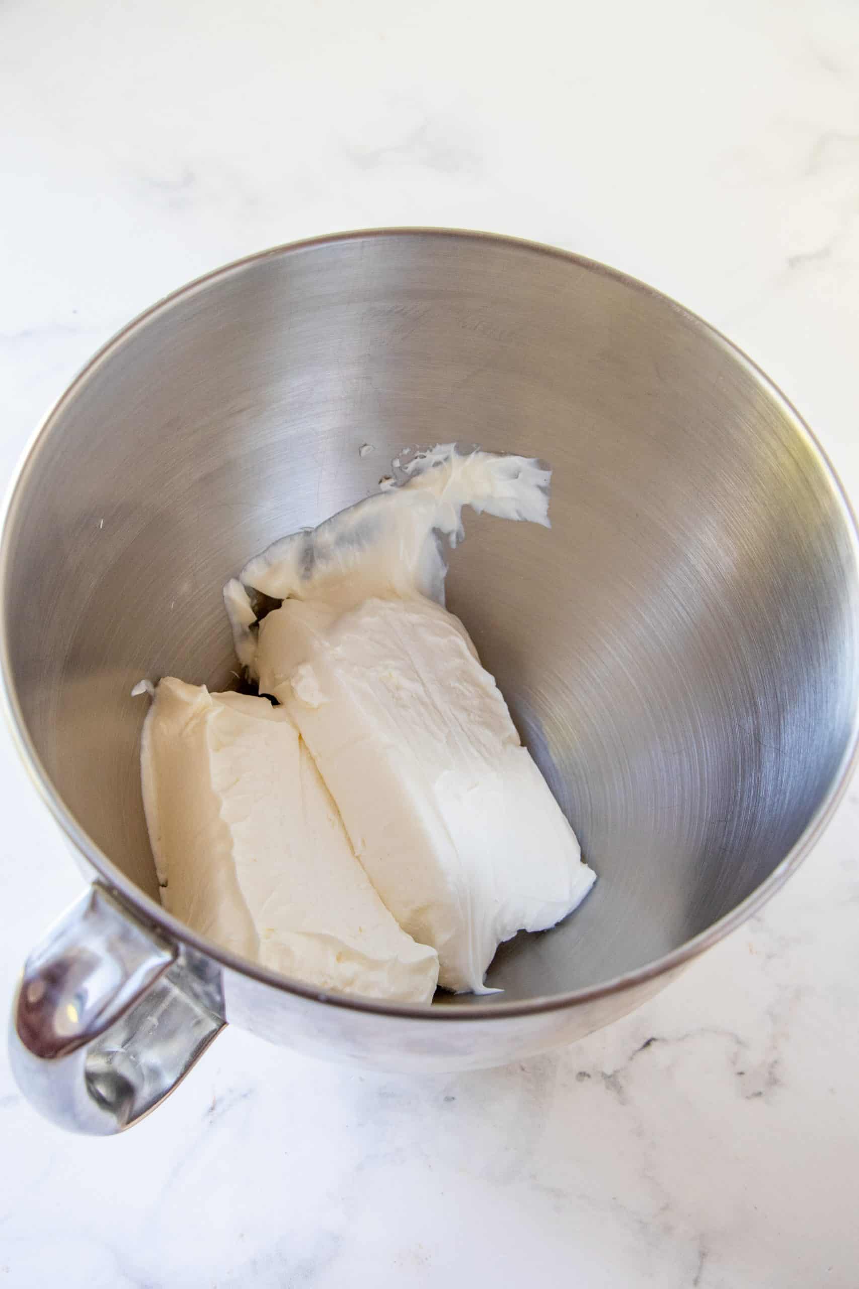 two blocks of cream cheese in the bottom of the bowl of a stand mixer.