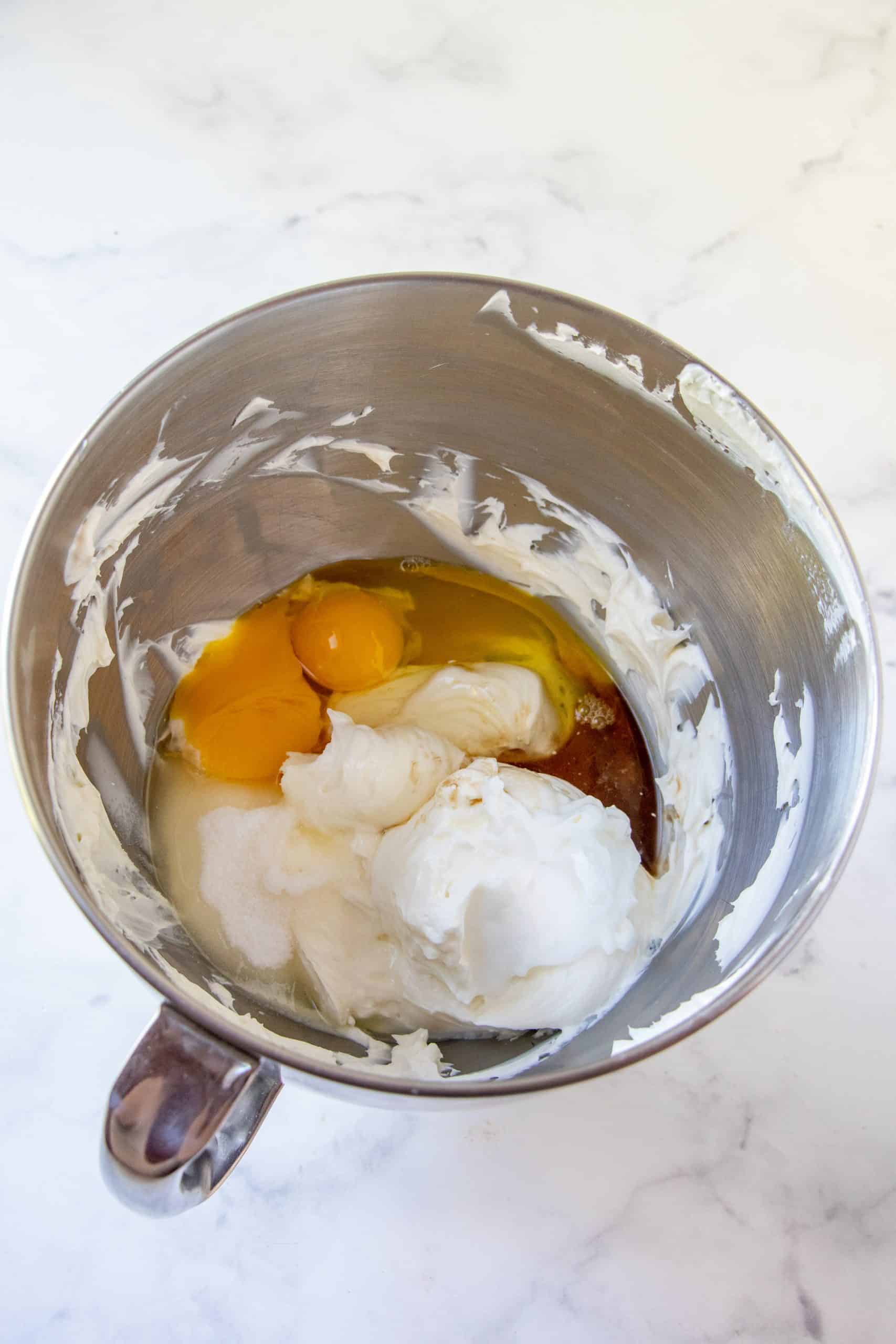 eggs, sour cream and vanilla extract added to cream cheese in a bowl.