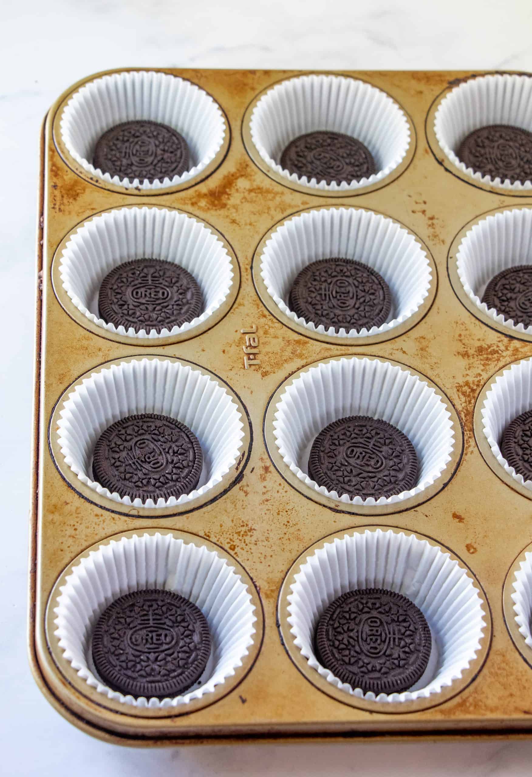 Oreo cookies placed into the bottom of paper cupcake liners in a muffin tin.