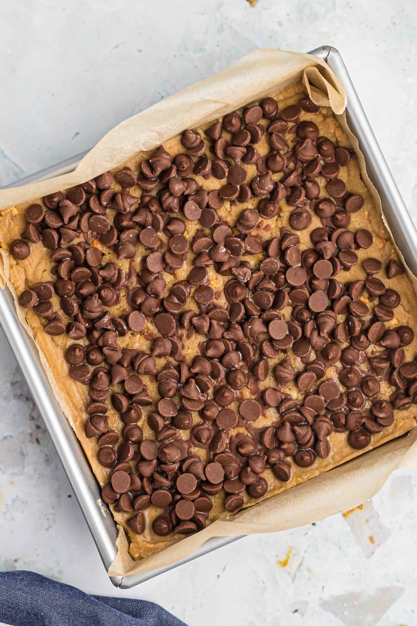 chocolate chips evenly sprinkled on top of peanut butter fudge in a baking pan.