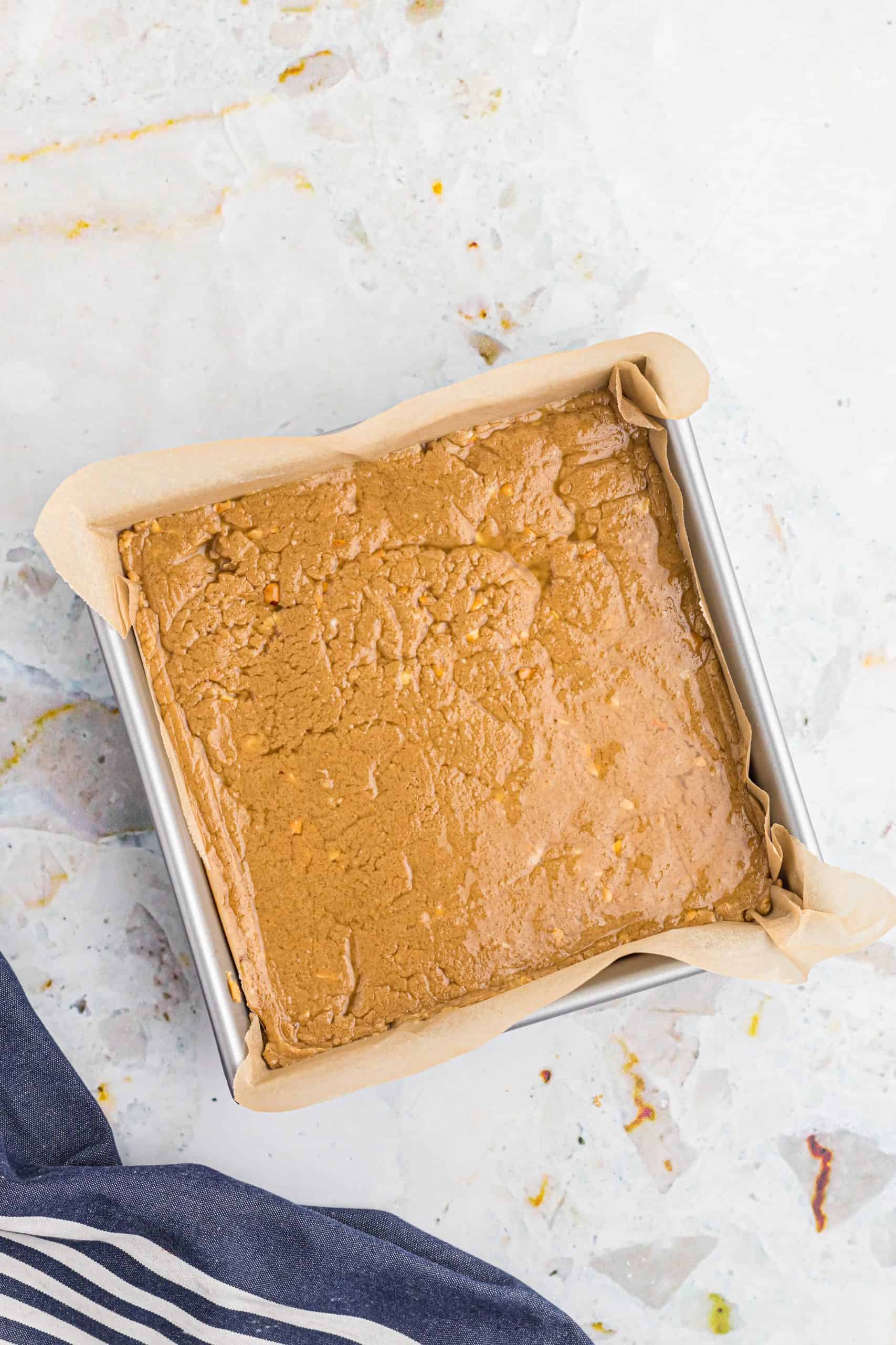 peanut butter fudge batter spread into a parchment paper line baking pan.