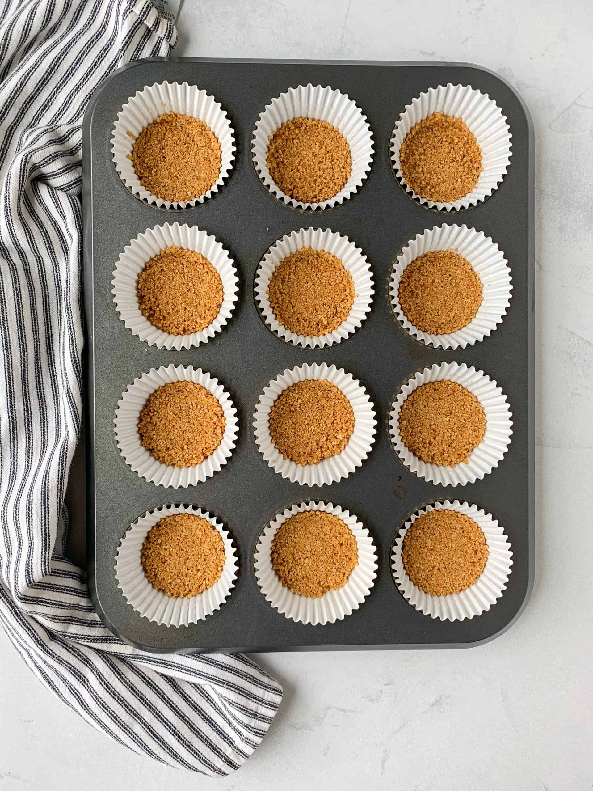 twelve cupcake paper liners filled with a graham cracker crust.