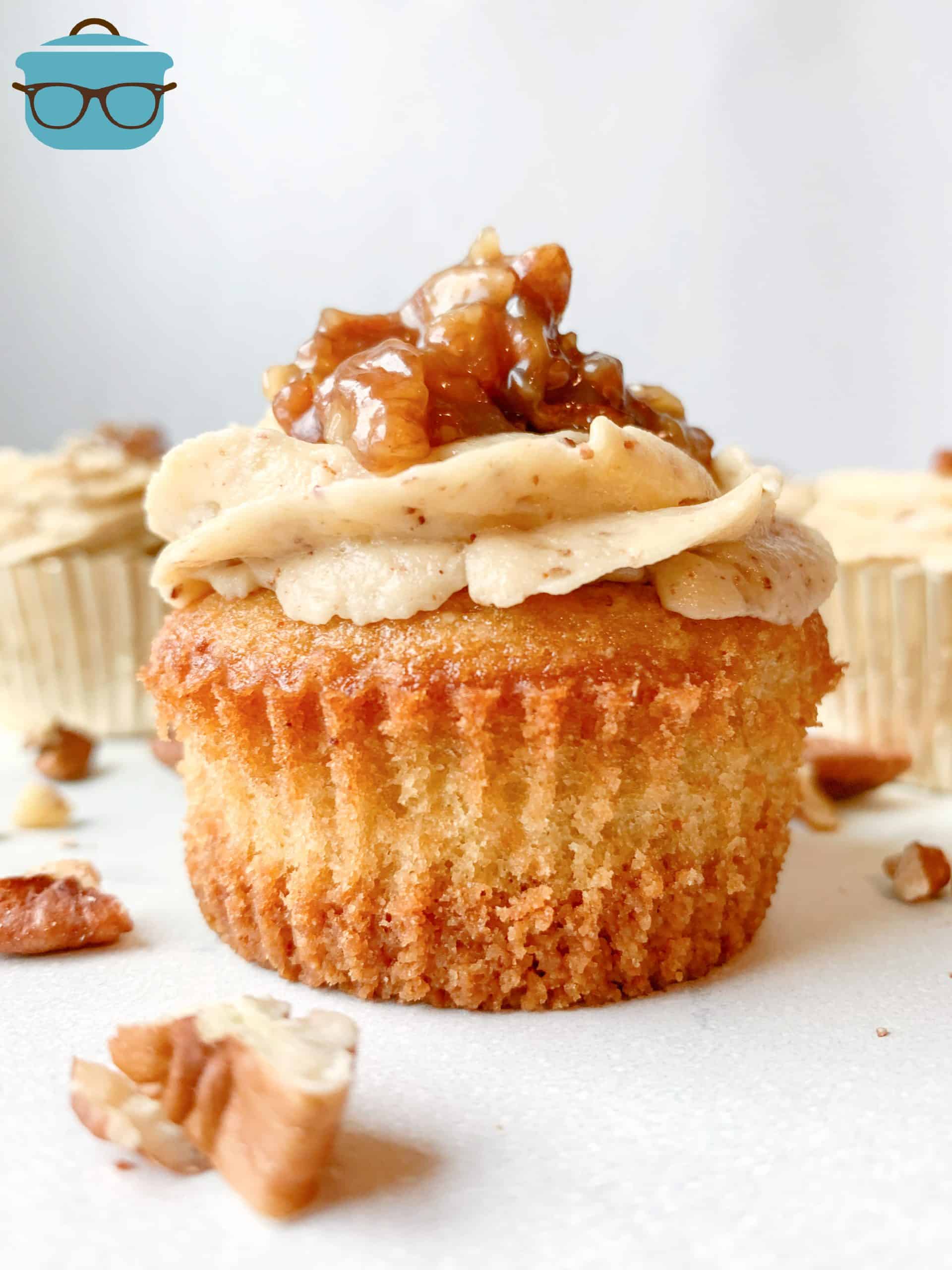 single pecan pie cupcake shown without a cupcake liner, chopped pecans sprinkled around the cupcake.