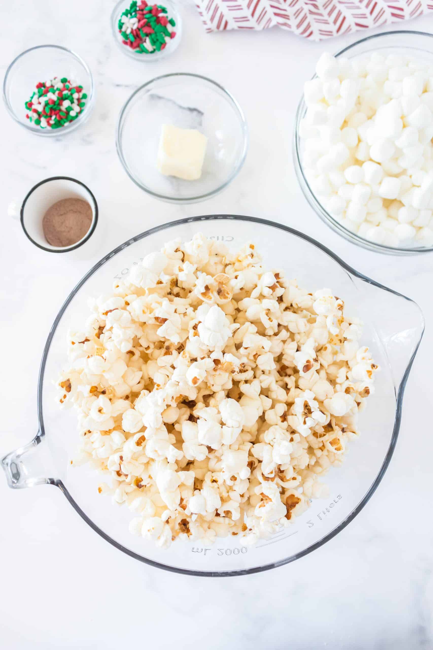 popped popcorn, butter, mini marshmallows, hot cocoa mix powder, Christmas sprinkles.