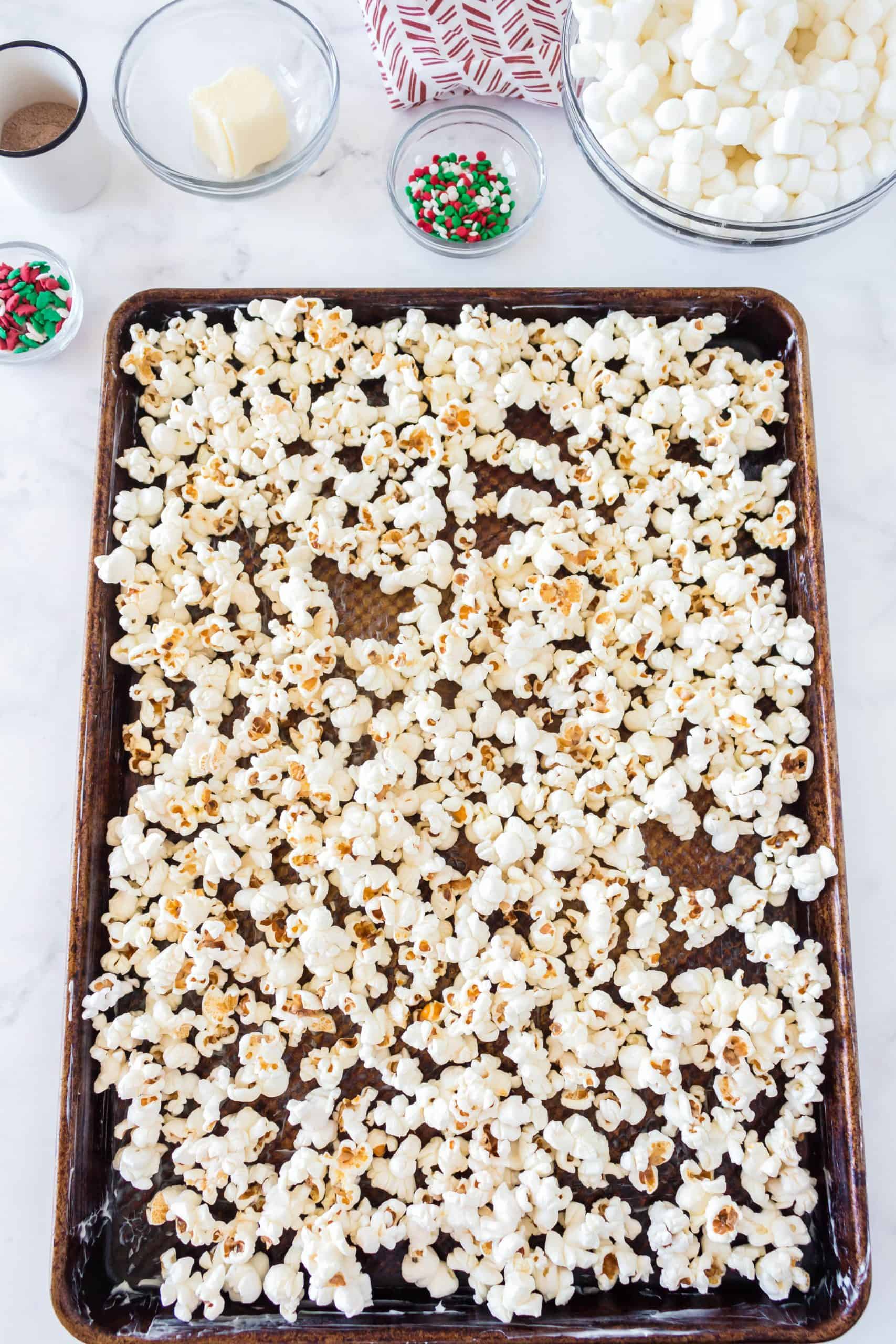 popped popcorn spread out onto butter coated baking sheet.