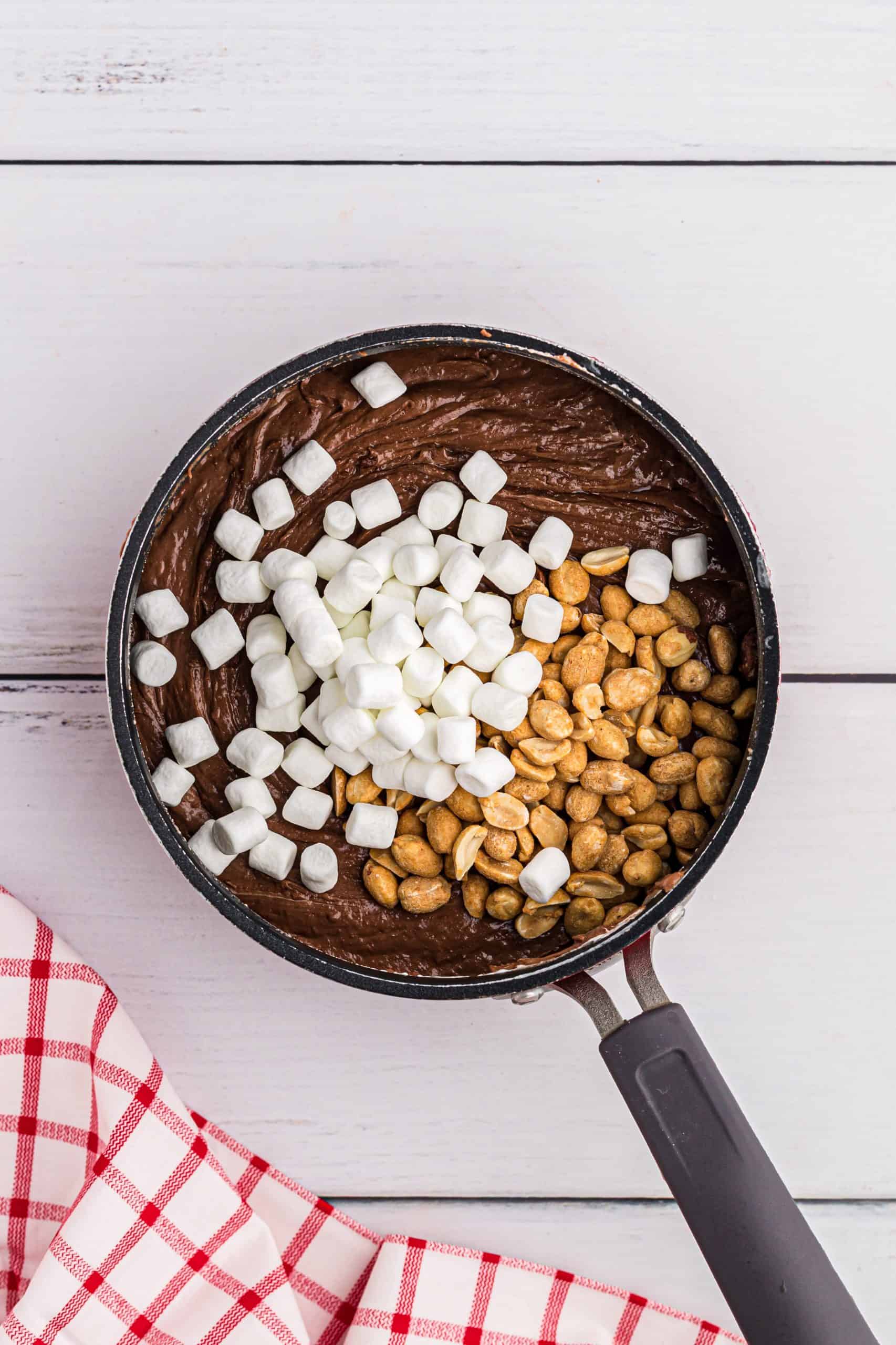 mini marshmallows and peanuts added to melted chocolate mixture in a sauce pan.