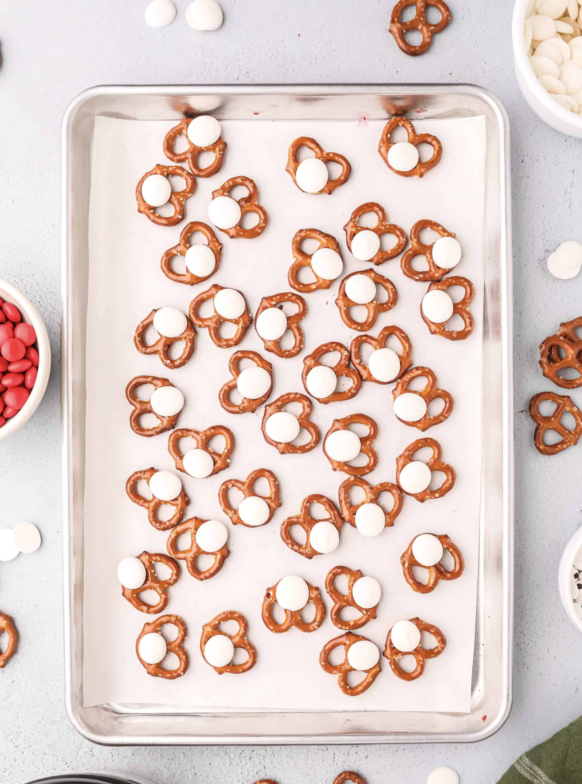 white candy pieces placed on each mini pretzel on a baking sheet.