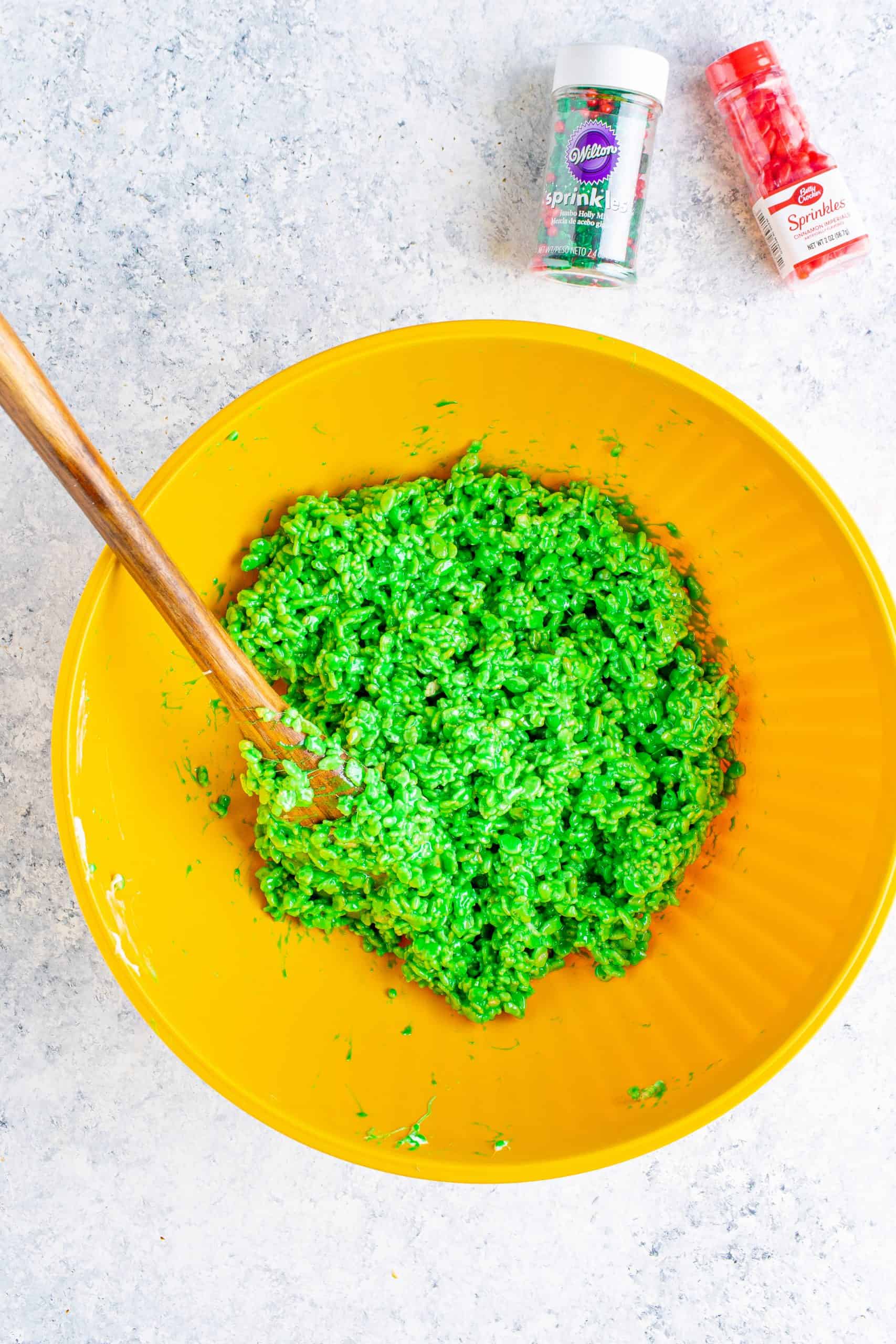 green rice krispies cereal in a large yellow bowl and a wooden spoon.