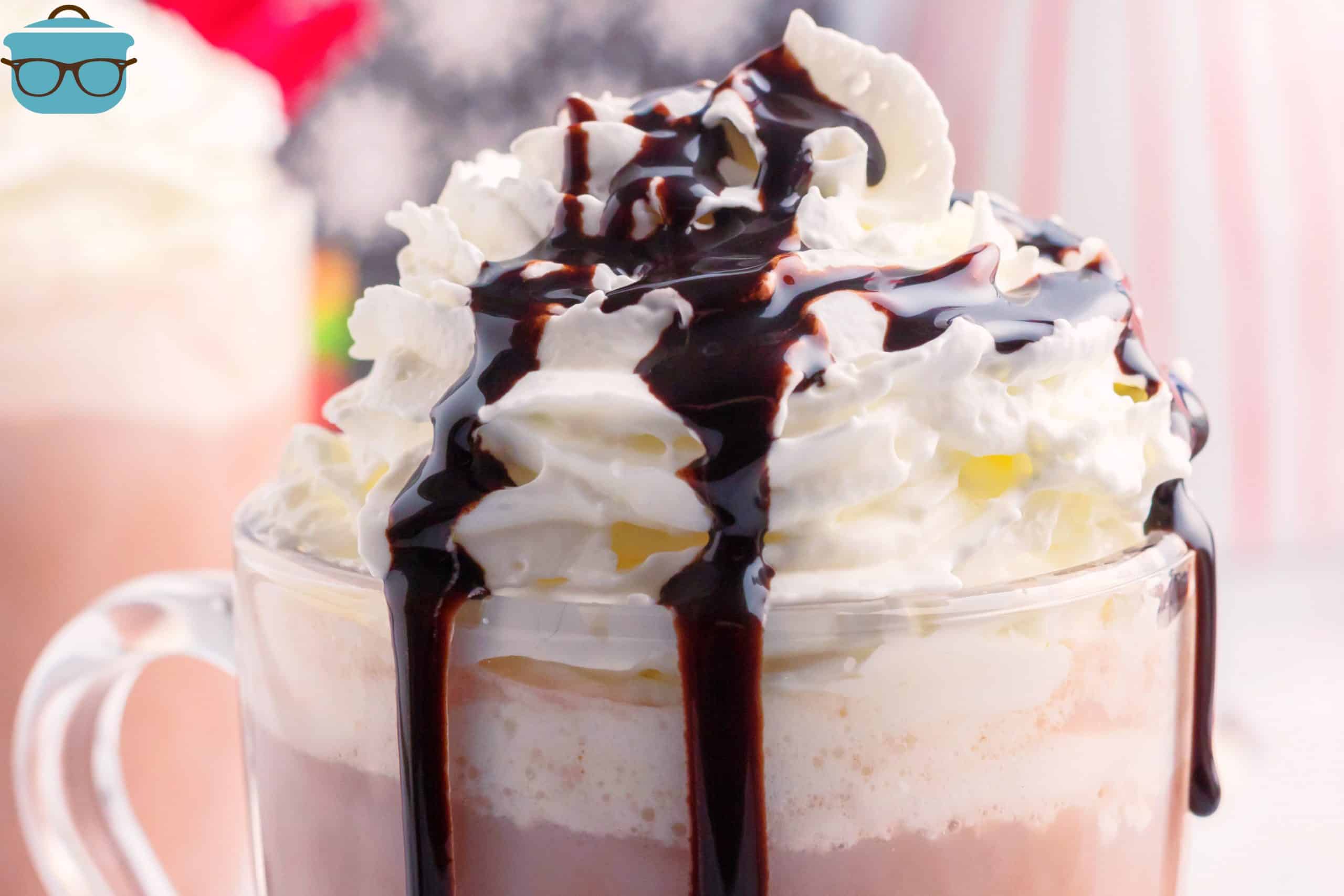 closeup of the top of a glass of hot cocoa topped with whipped cream and chocolate syrup.