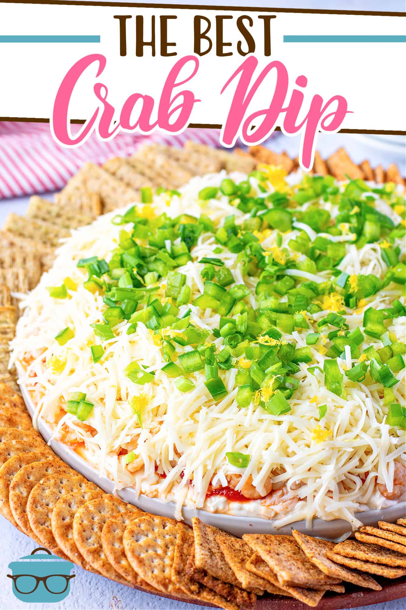 The Best Crab Dip recipe from The Country Cook, dip shown on a round white platter, topped with sliced green onions with crackers arranged in a circle around the dip.
