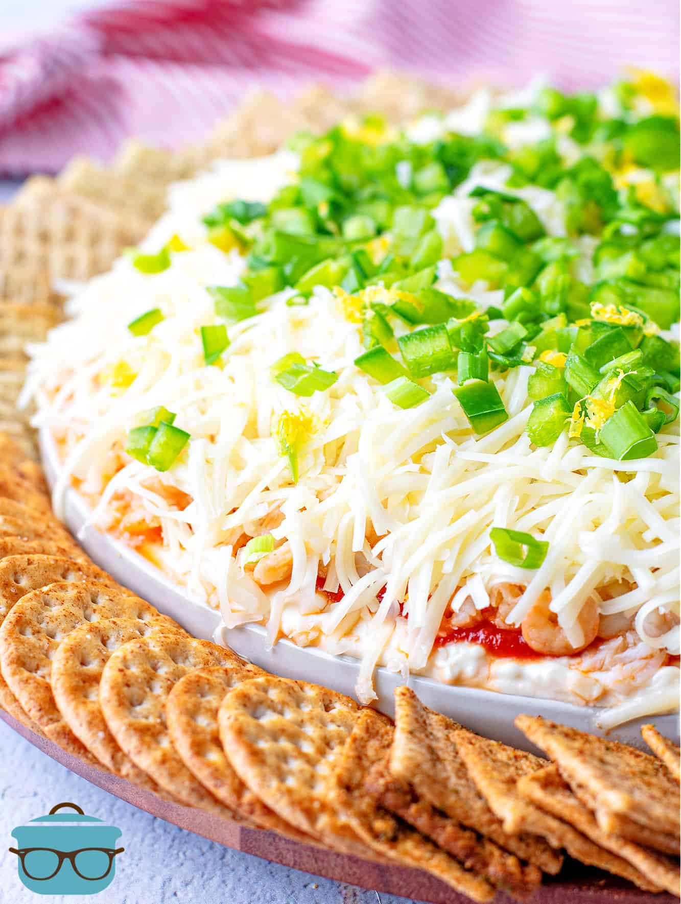 closeup photo of seafood dip topped with sliced green onions and crackers surrounding the platter in a circle.