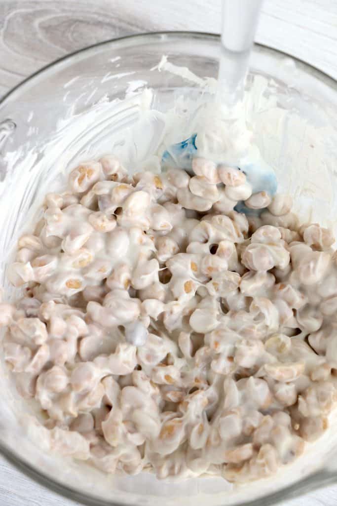 peanuts stirred together with vanilla almond bark candy coating in a clear bowl.