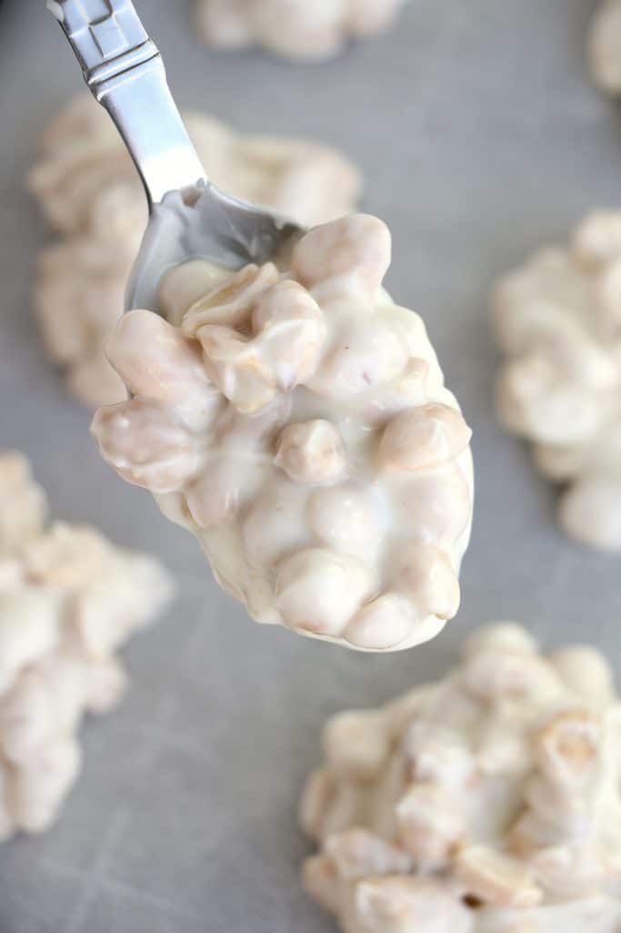 spoonful of white chocolate and peanut mixture held over a baking sheet with other peanut clusters spread across.