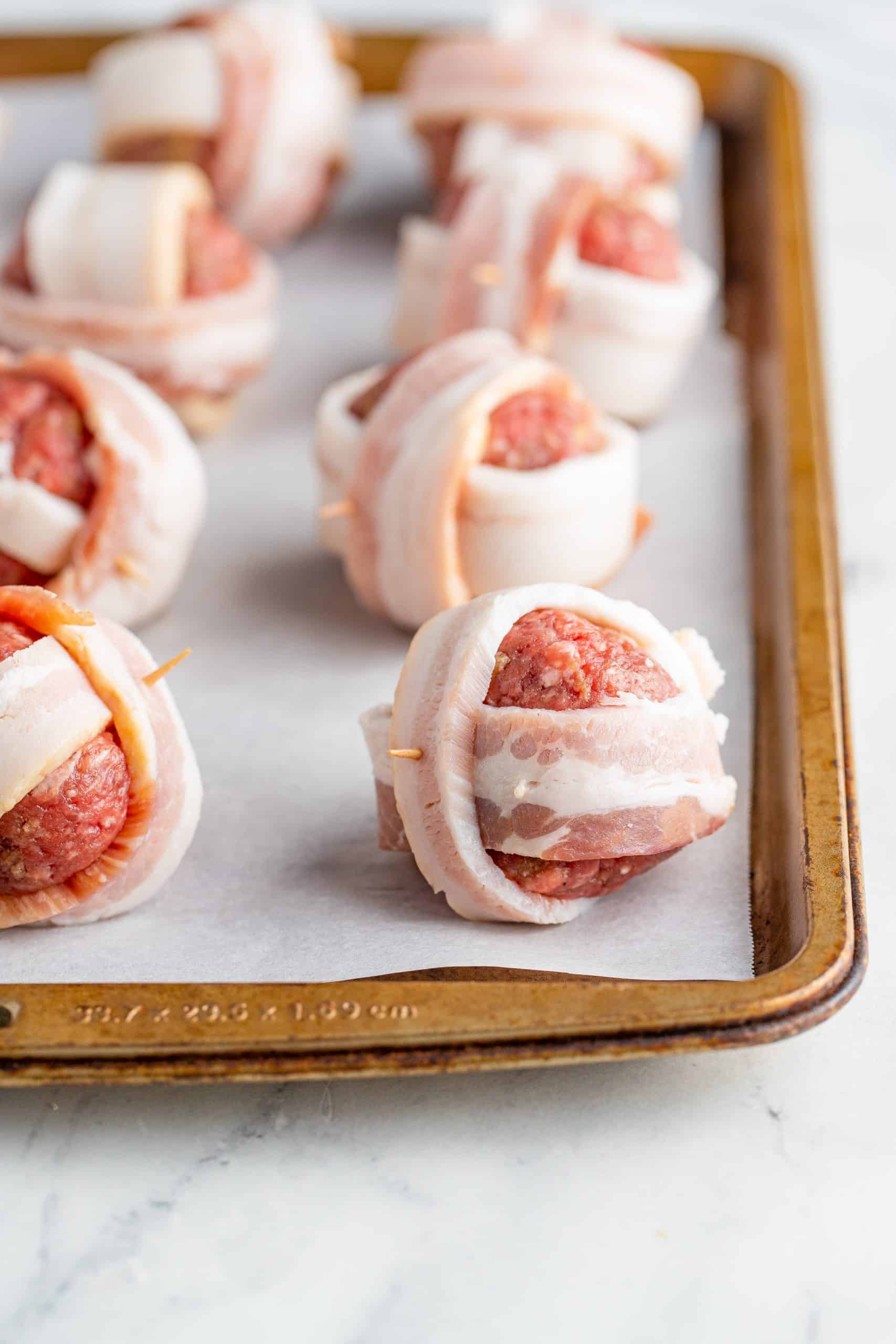 Meatballs on parchment lined baking sheet wrapped in bacon.