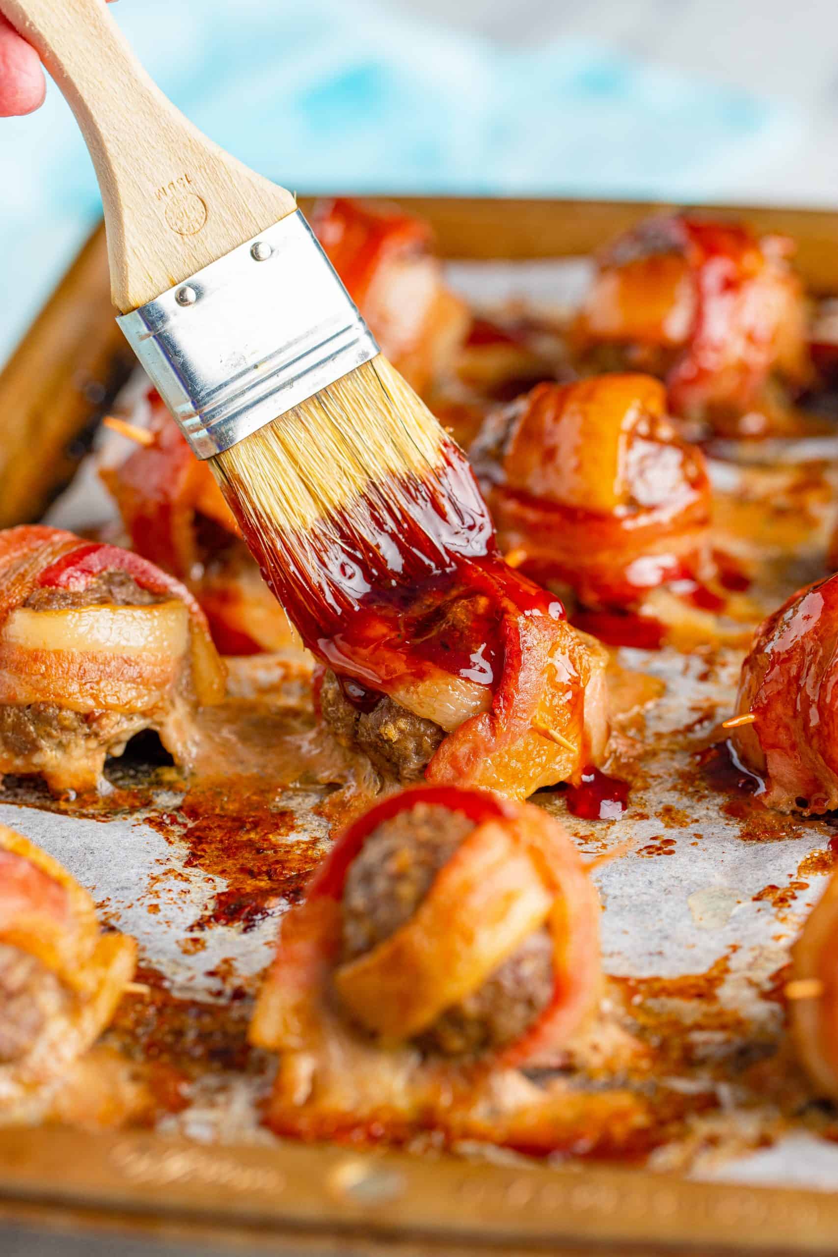 BBQ sauce mixture being brushed on bacon wrapped meatballs.