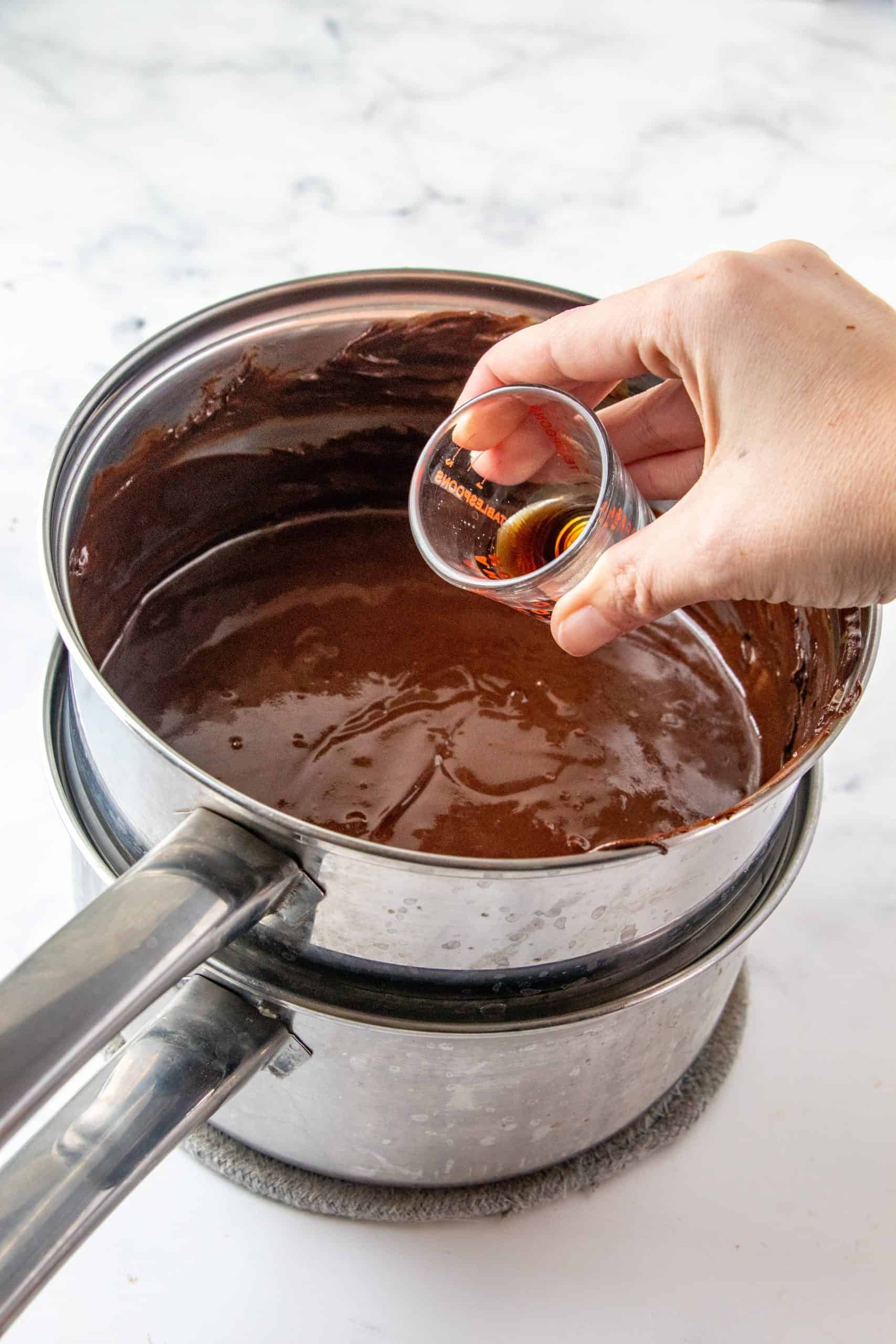 Vanilla being poured into melted chocolate in double boiler.