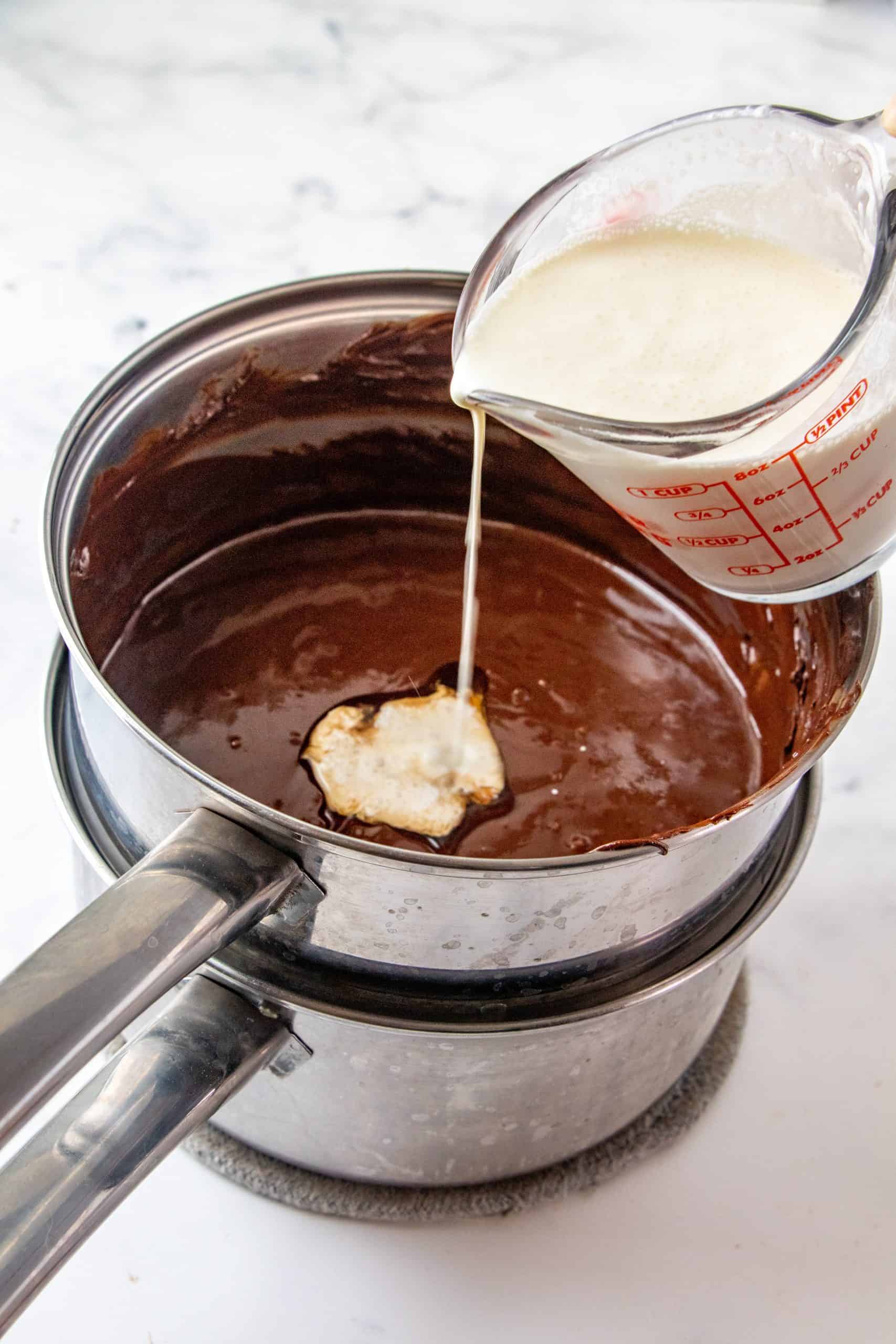 Heavy cream being poured into chocolate sauce in a pan.