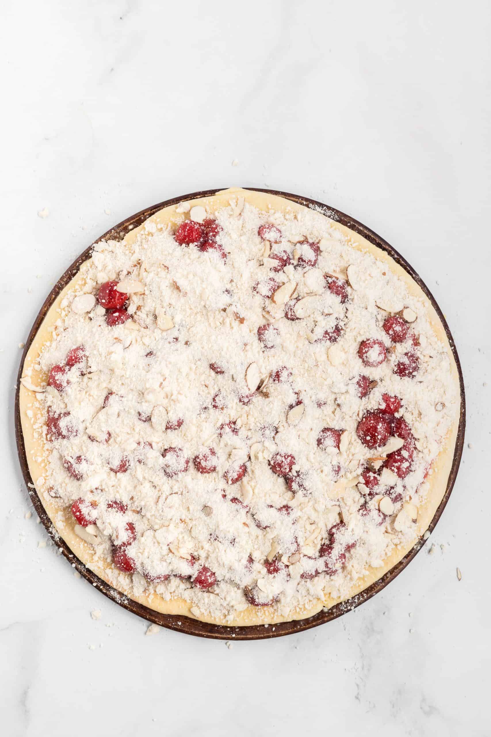 streusel topping with almonds sprinkled on top of cherry pie filling on pizza dough. 