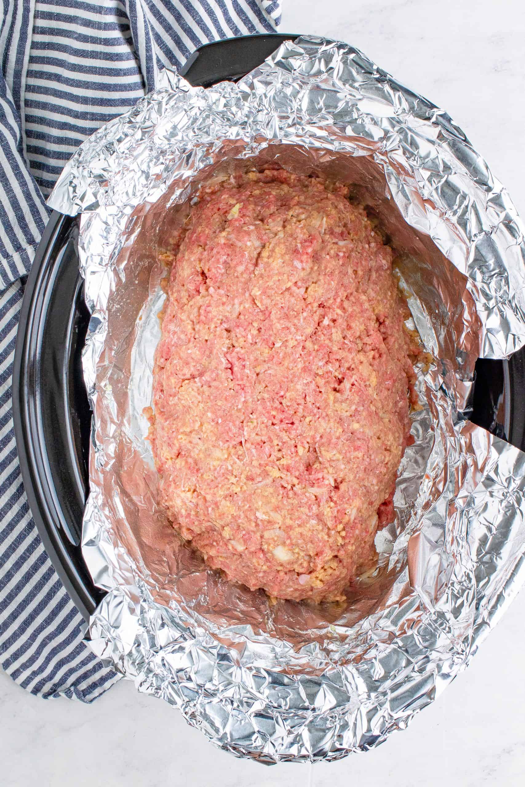 Ground beef shaped into a loaf in a foil lined crock pot