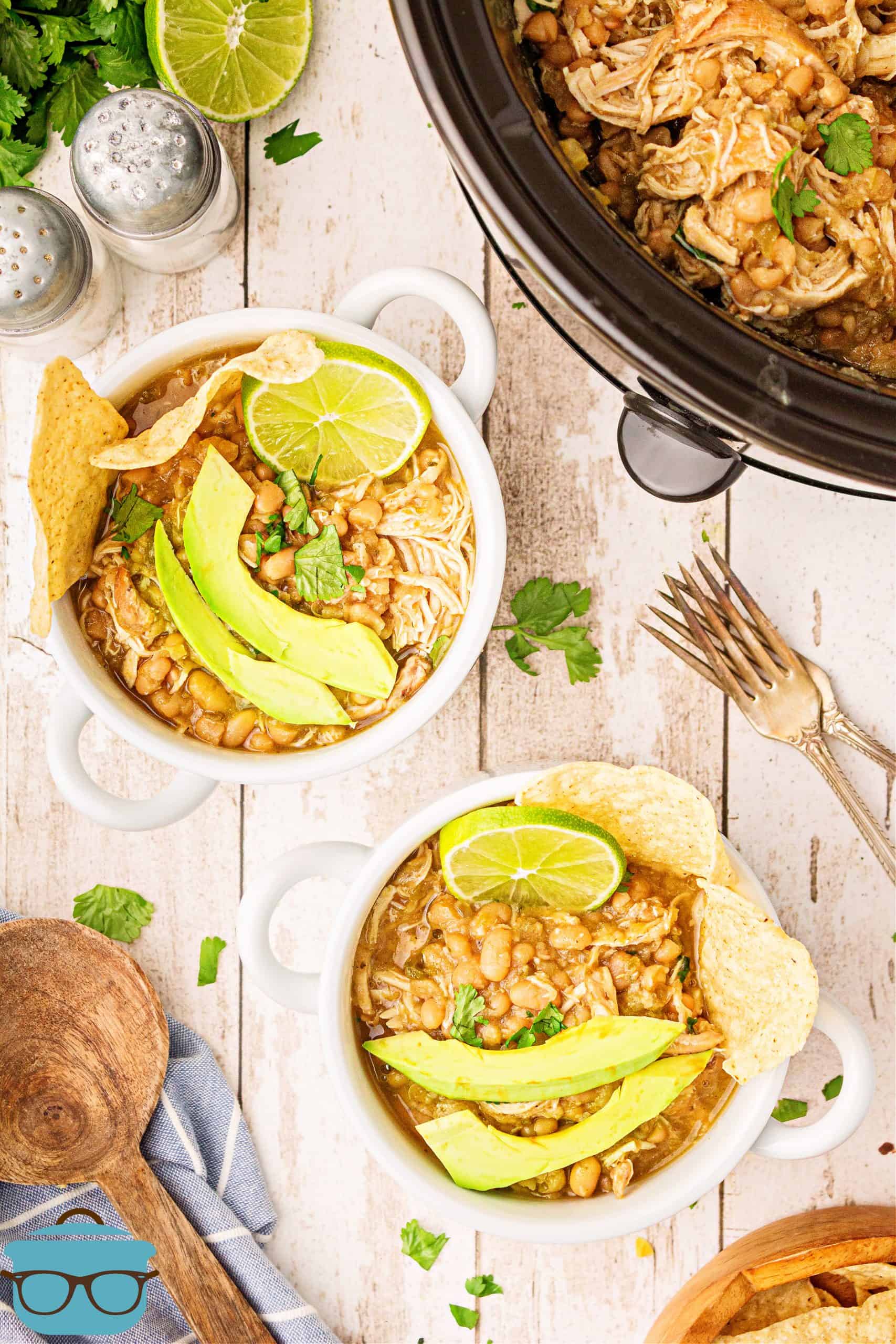 Overhead of two bowls of Crock Pot White Chicken Chili topped with avocado, limes and chips.