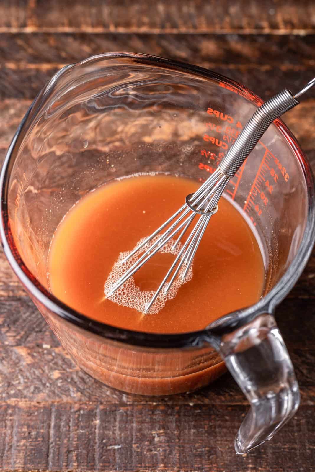 beef broth, tomato paste and mustard mixed together with a whisk in a measuring cup. 