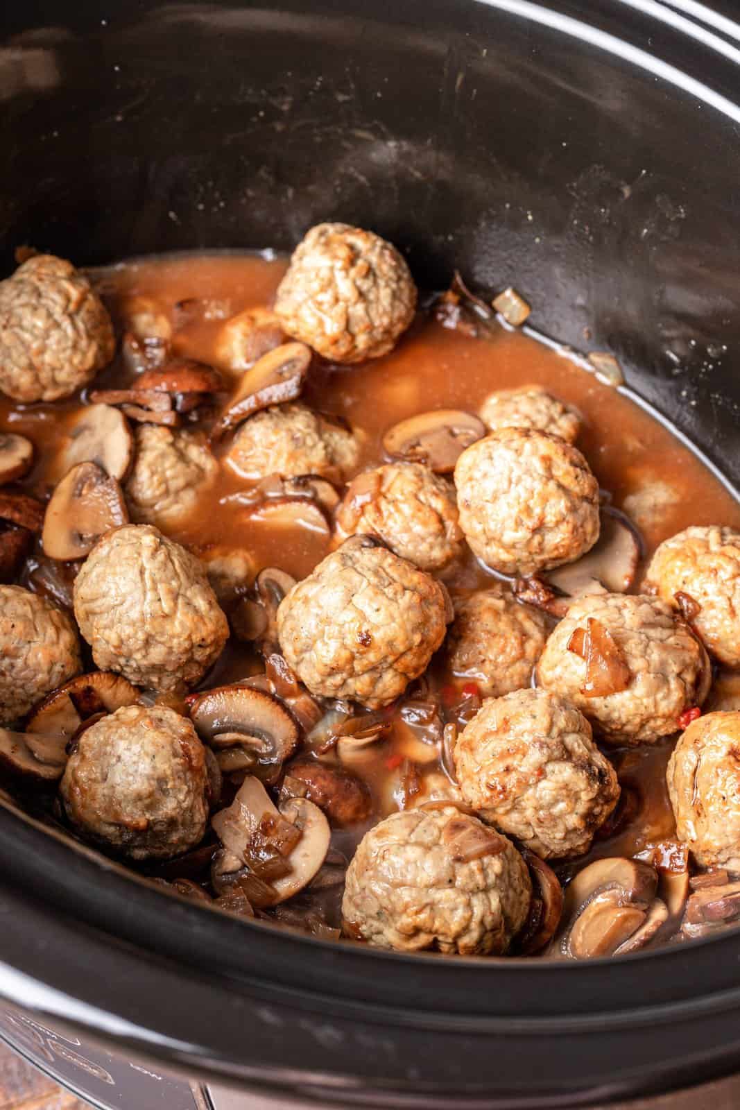 beef broth mixture added to meatballs in oval slow cooker. 